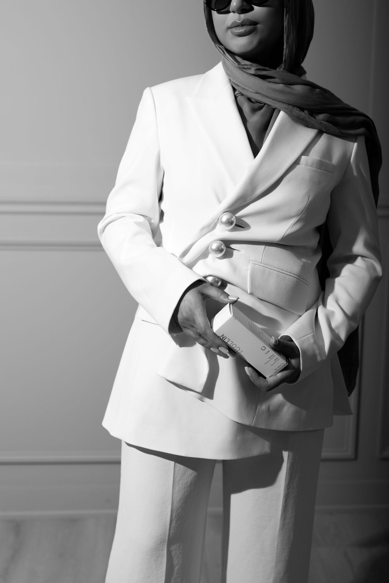A stylish monochrome fashion photo showing someone in a crisp white pantsuit and hijab holding an elegant clutch purse.