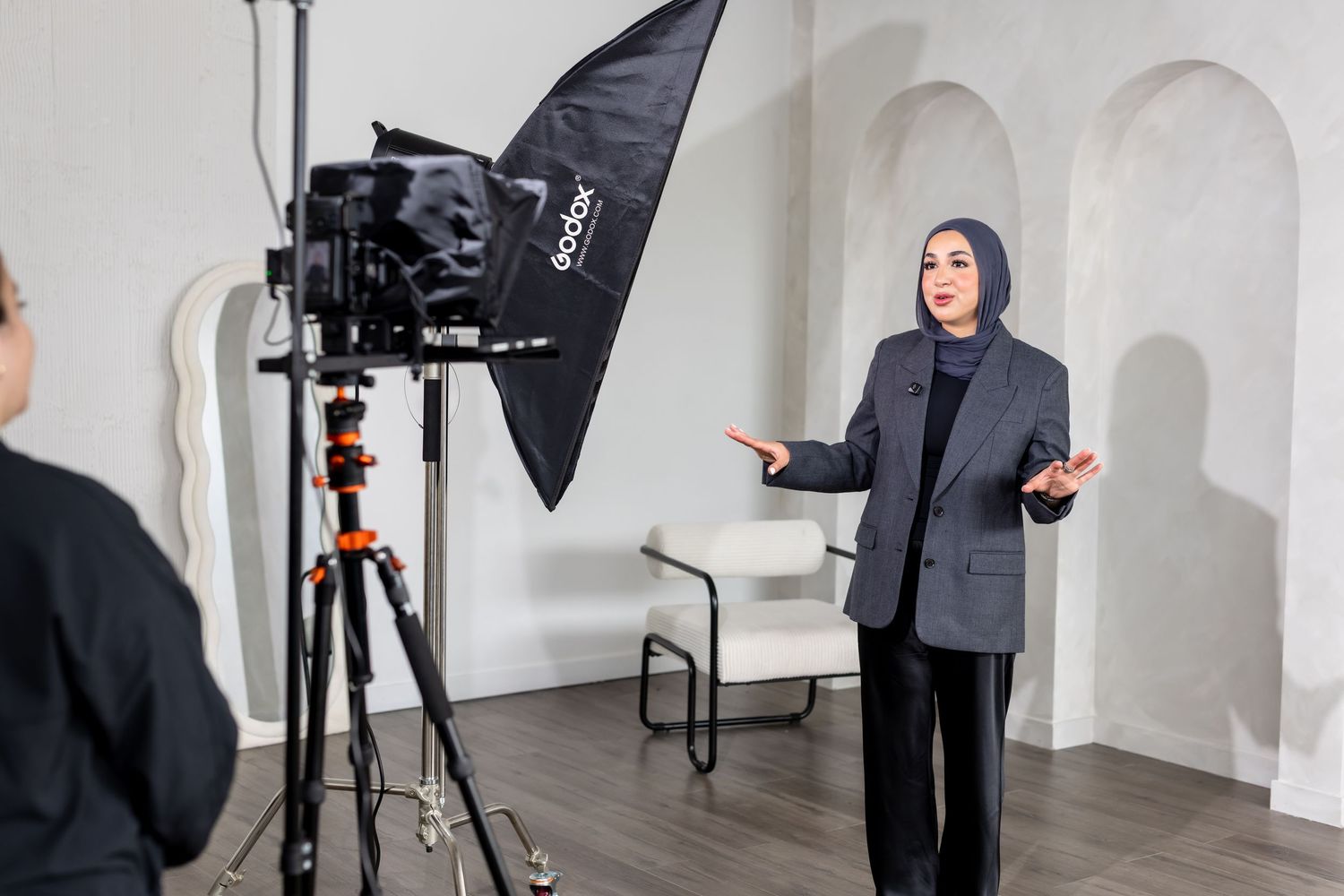 Professional photographer adjusts lighting equipment and camera setup in a white studio space during photoshoot.