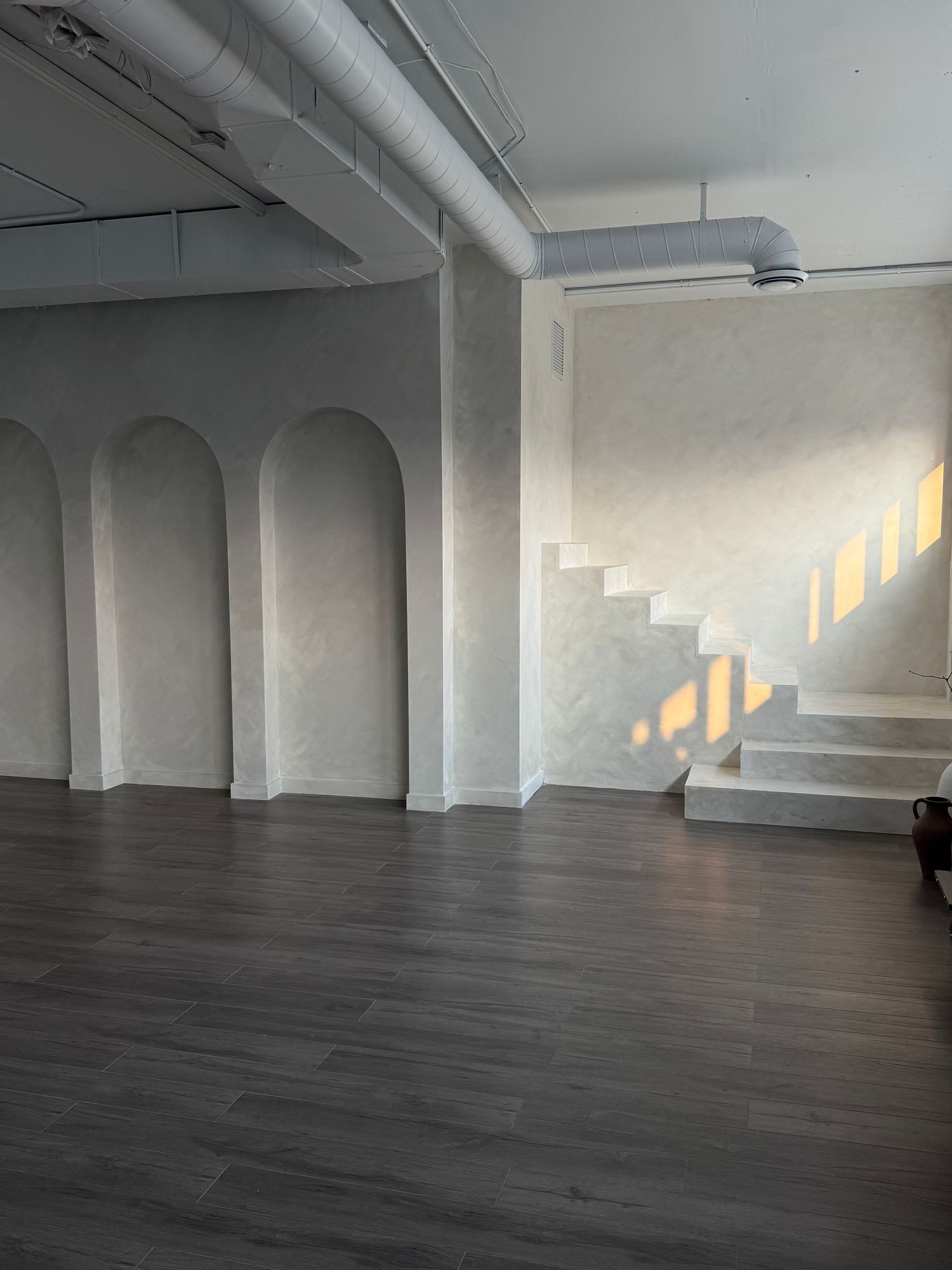 Modern minimalist studio space with arched windows and dark hardwood floors bathed in natural light.