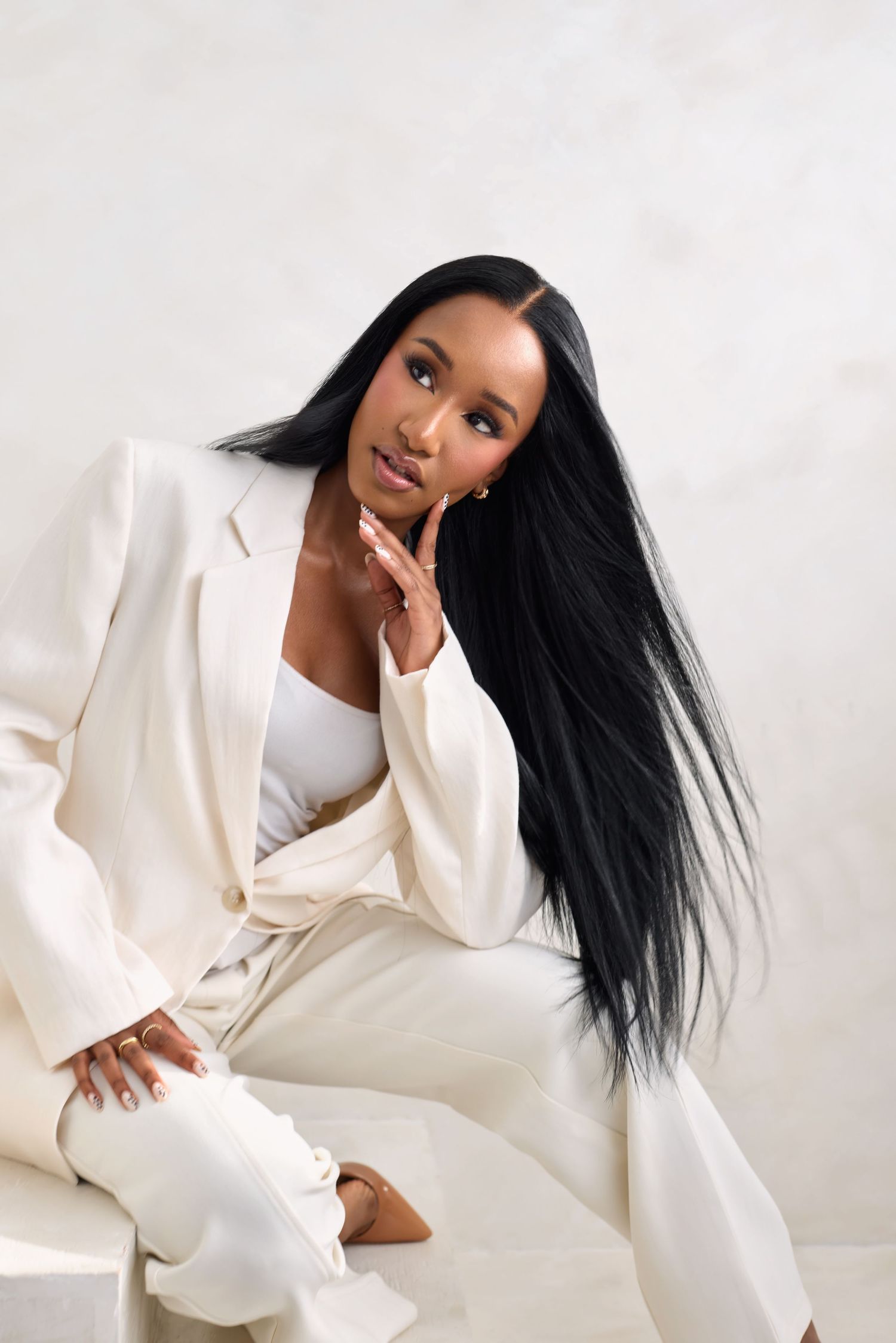 Fashion model in all-white ensemble poses elegantly against light background in professional photoshoot series.