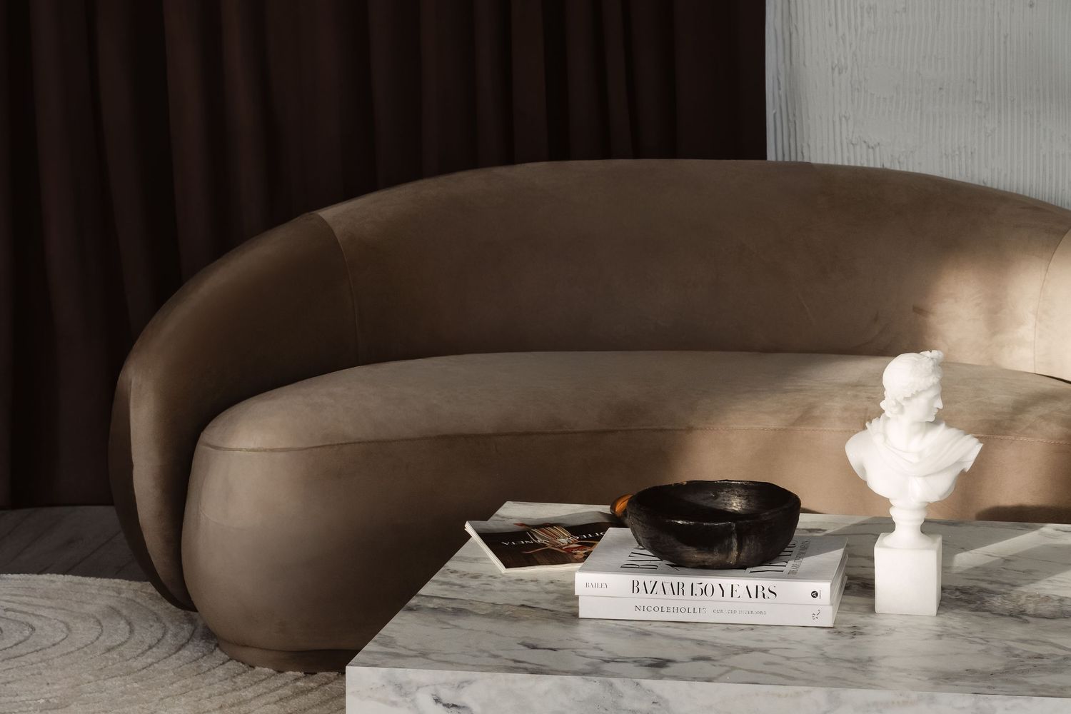 A modern living room interior with neutral tones features a curved sofa, coffee table, and decorative candles.