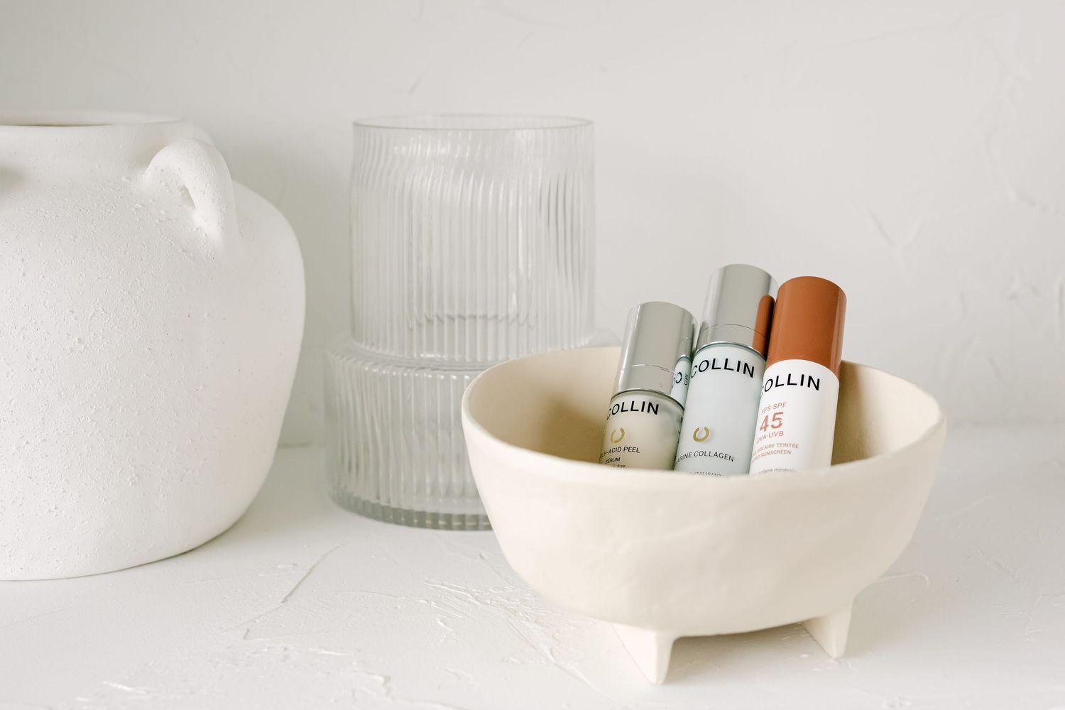 A minimalist scene with white ceramic bowls and rolled items against a light background with a textured glass vase.