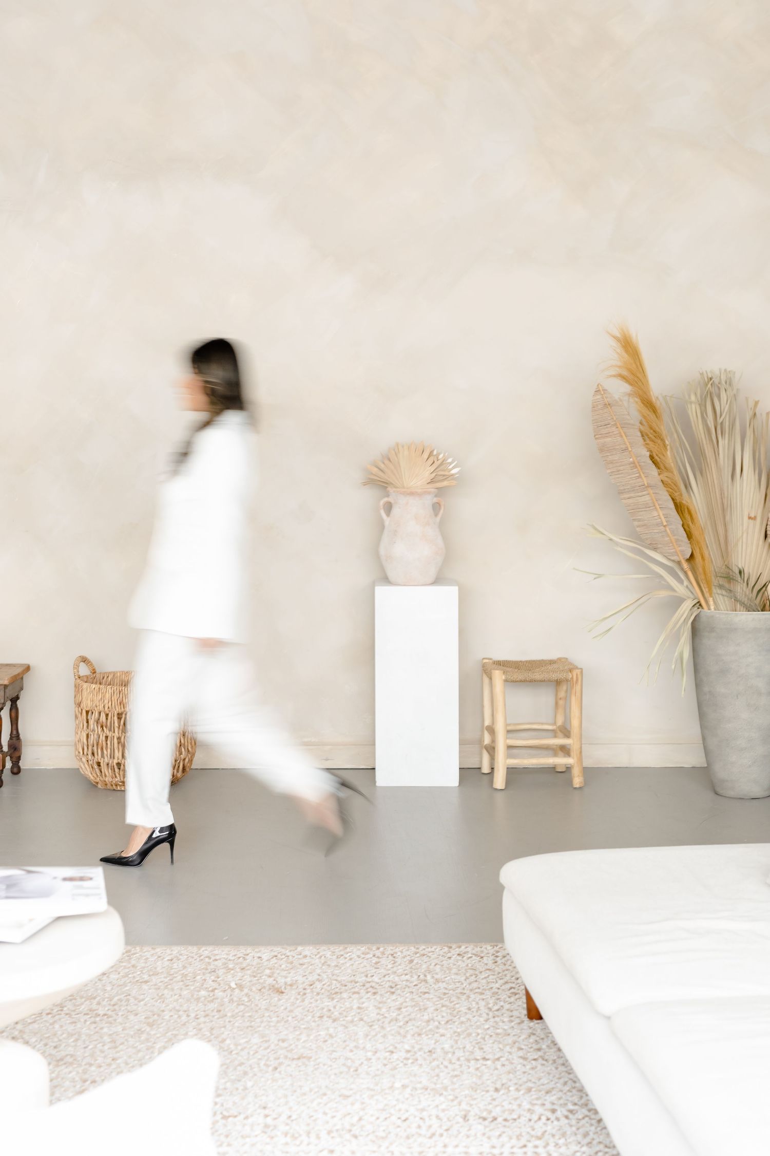 Simple studio setting with a minimalist white space featuring dried floral arrangements and wooden furniture against a wall.
