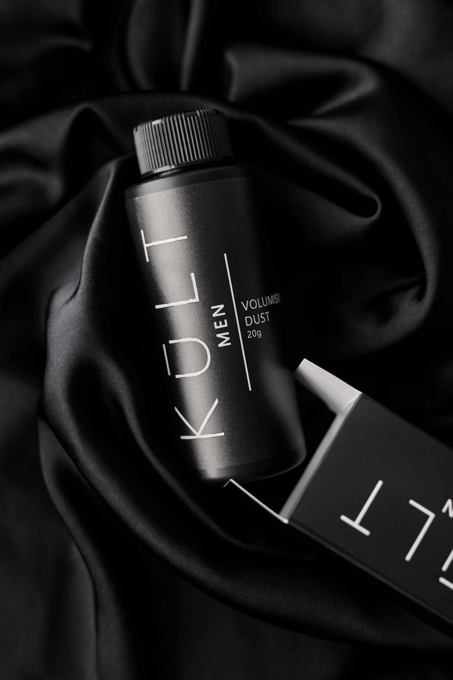 Close-up shot of black minimalist K.I.T. beauty product packaging against dark fabric background.