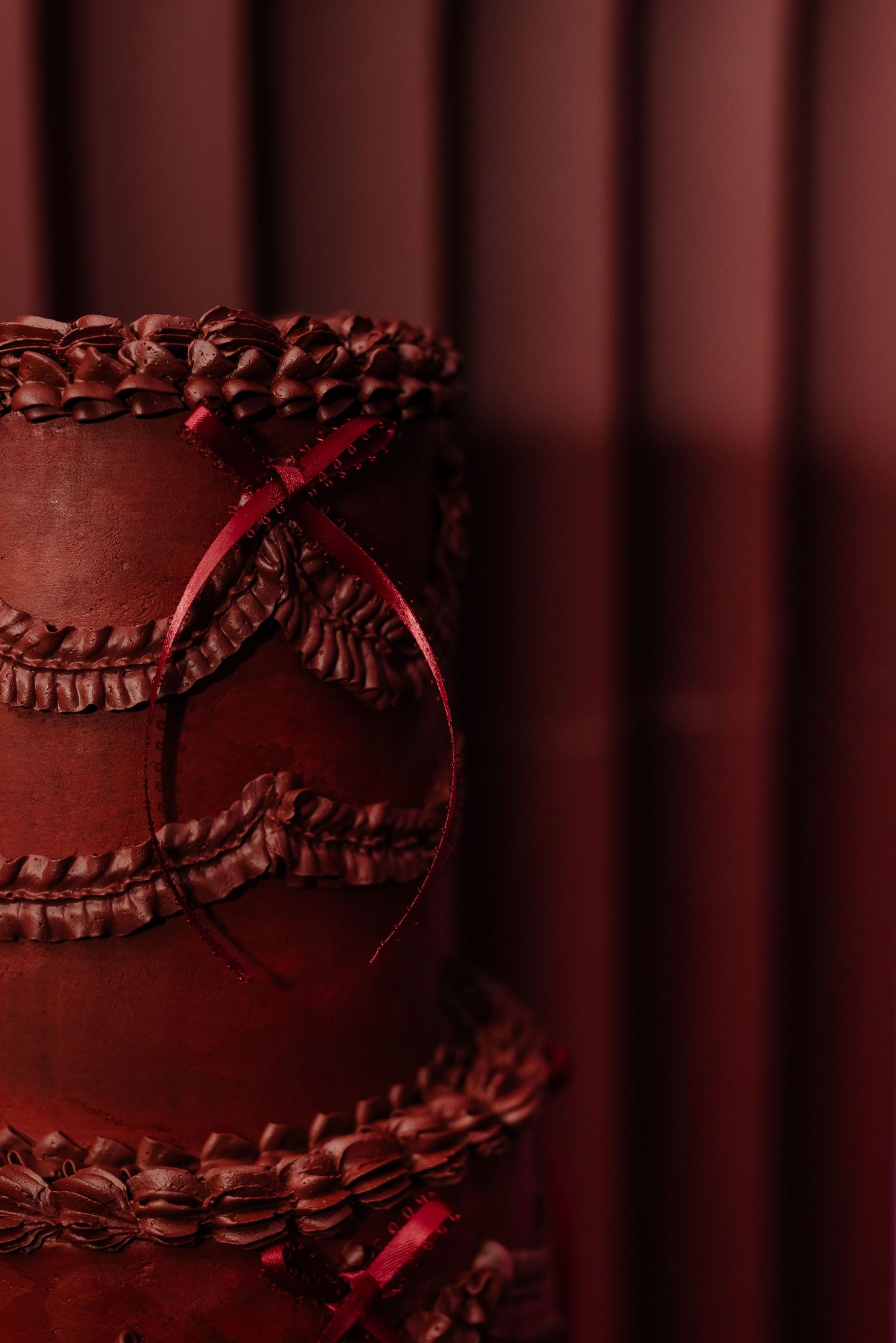 Elegant dark red multi-tiered chocolate cake with ruffled layers and ribbon decoration against a deep crimson background.