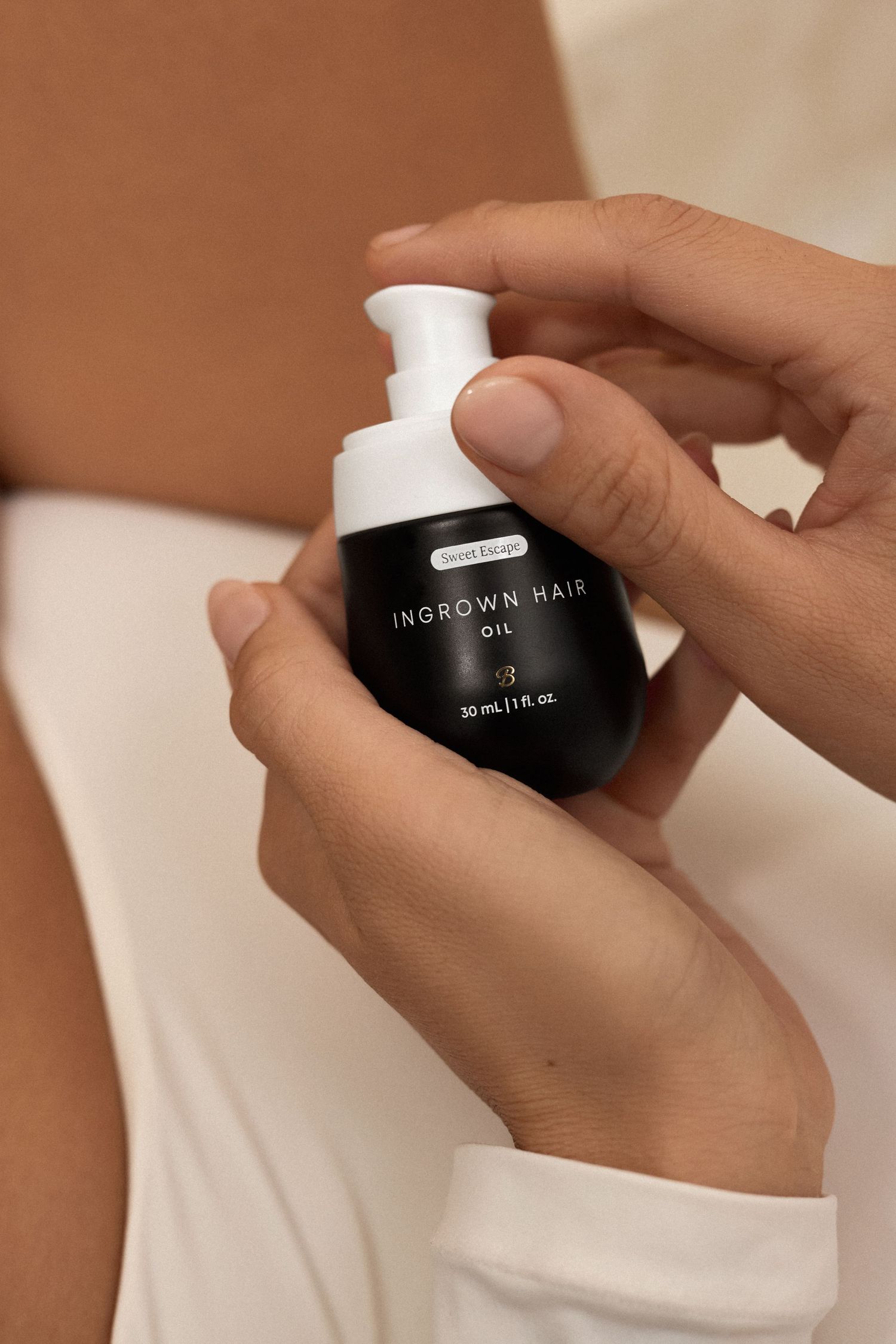Hands holding a small black bottle of ingrown hair gel against a beige background.