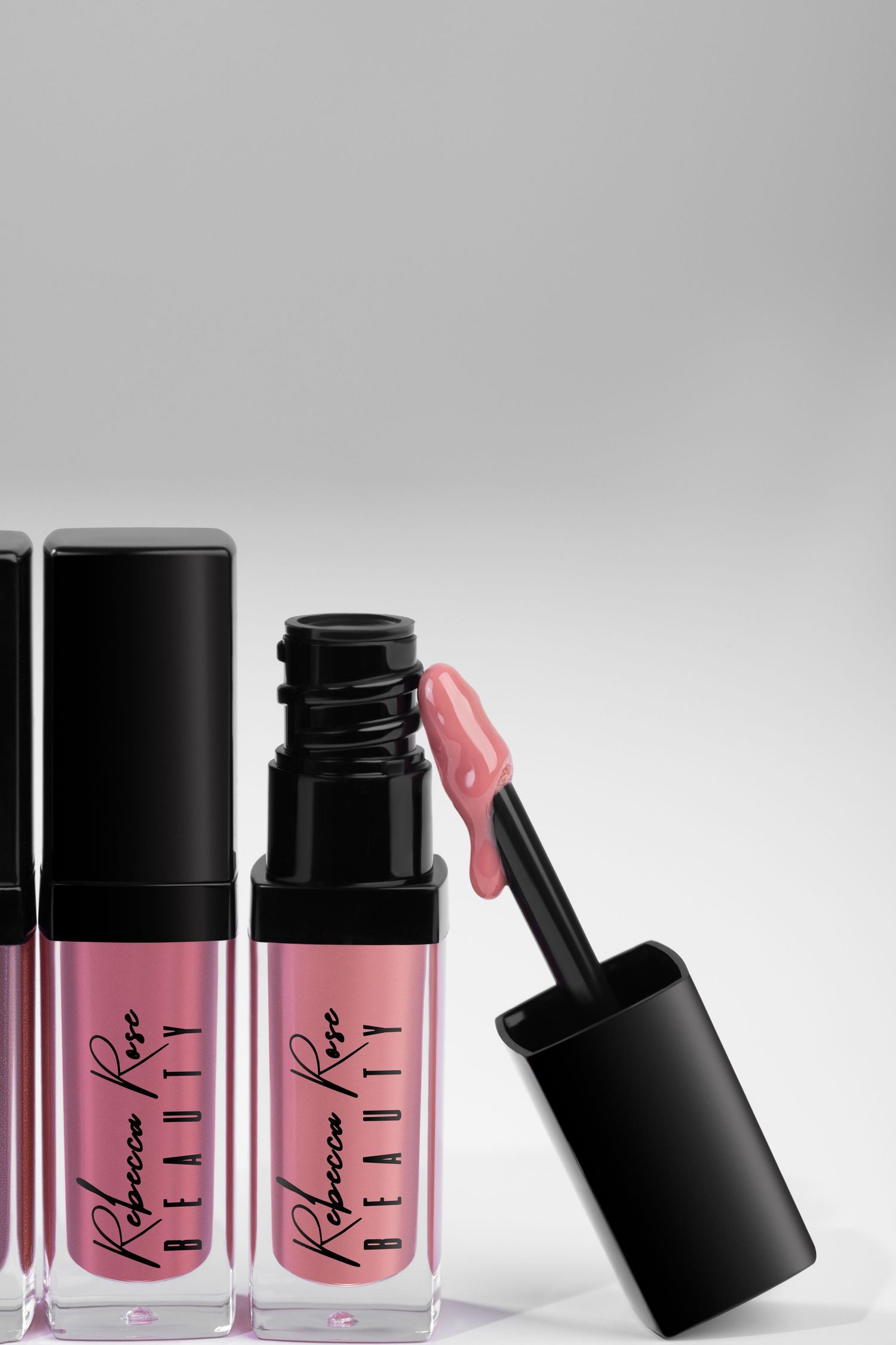 Two pink liquid lipstick bottles with black caps and applicator wands against a light gray background.