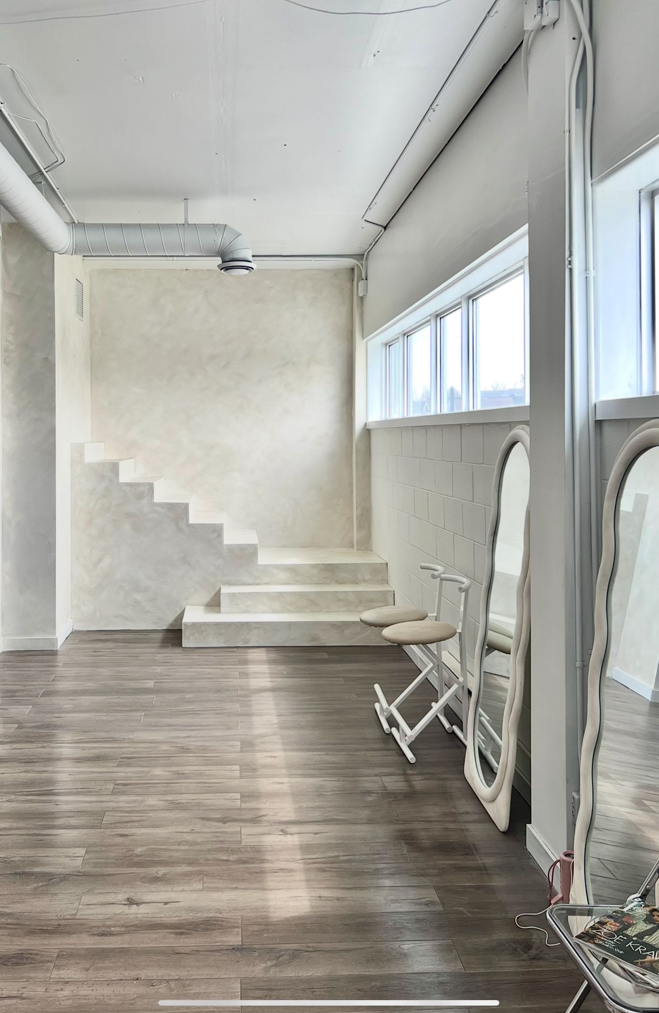 Bright studio interior with white stairs, exposed ductwork, and full-length mirrors.