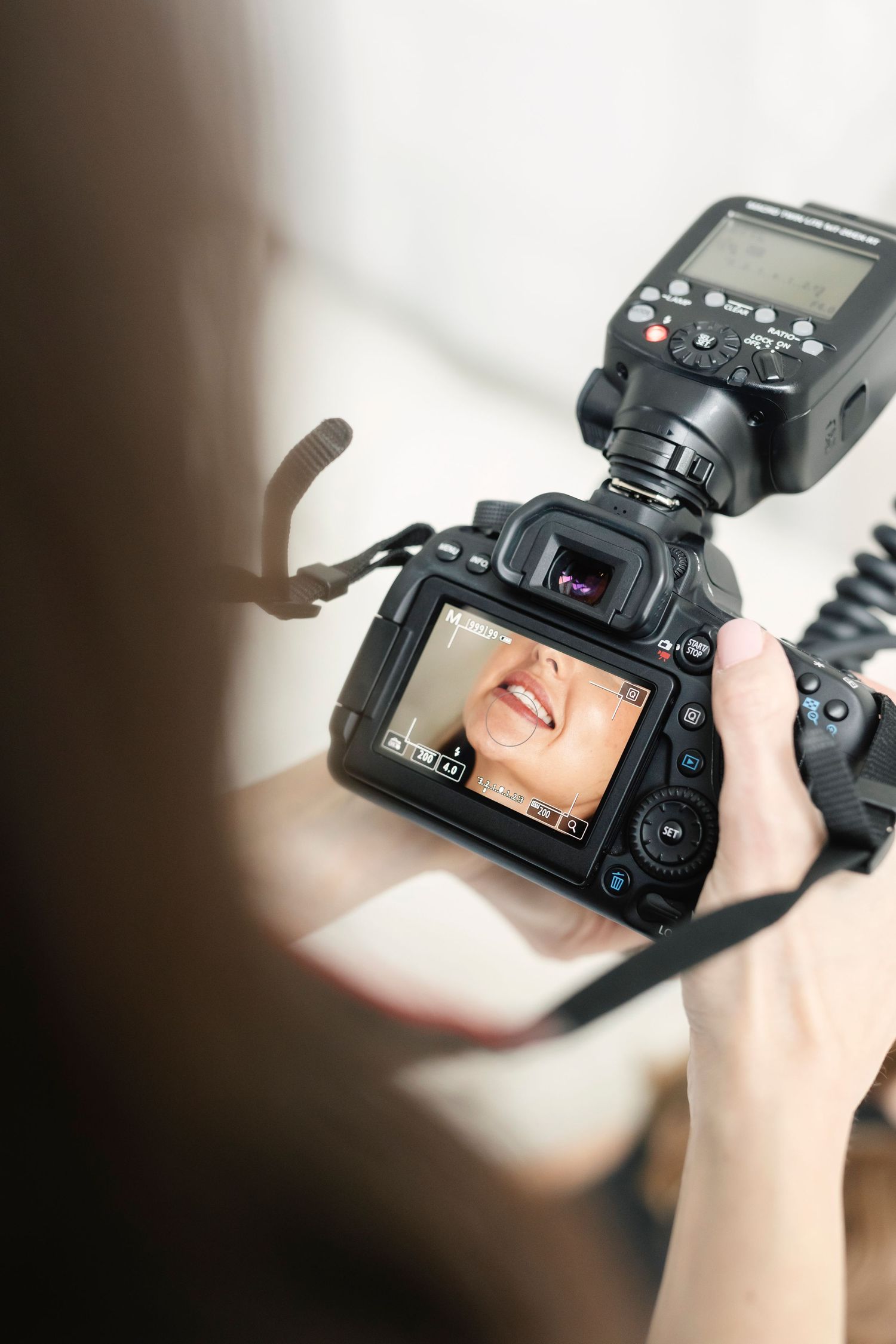 Photographer holds DSLR camera with external flash, reviewing a close-up portrait shot on the LCD screen.