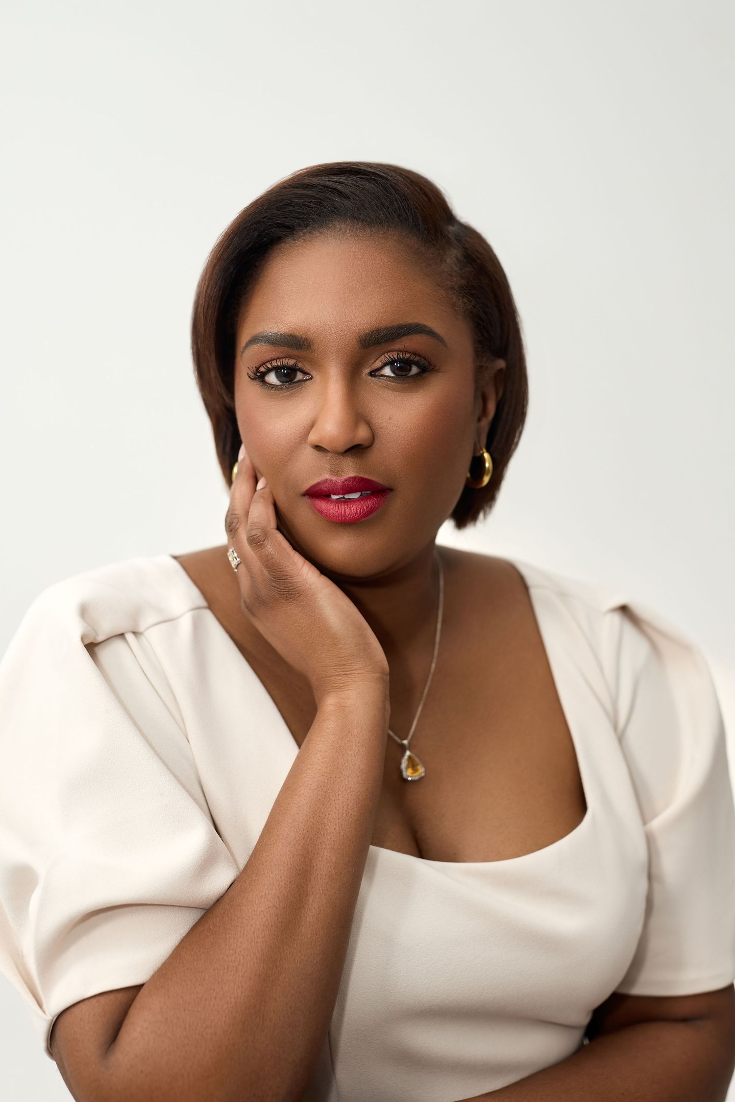 Professional portrait photo of someone wearing a white top against a light background in an elegant pose.