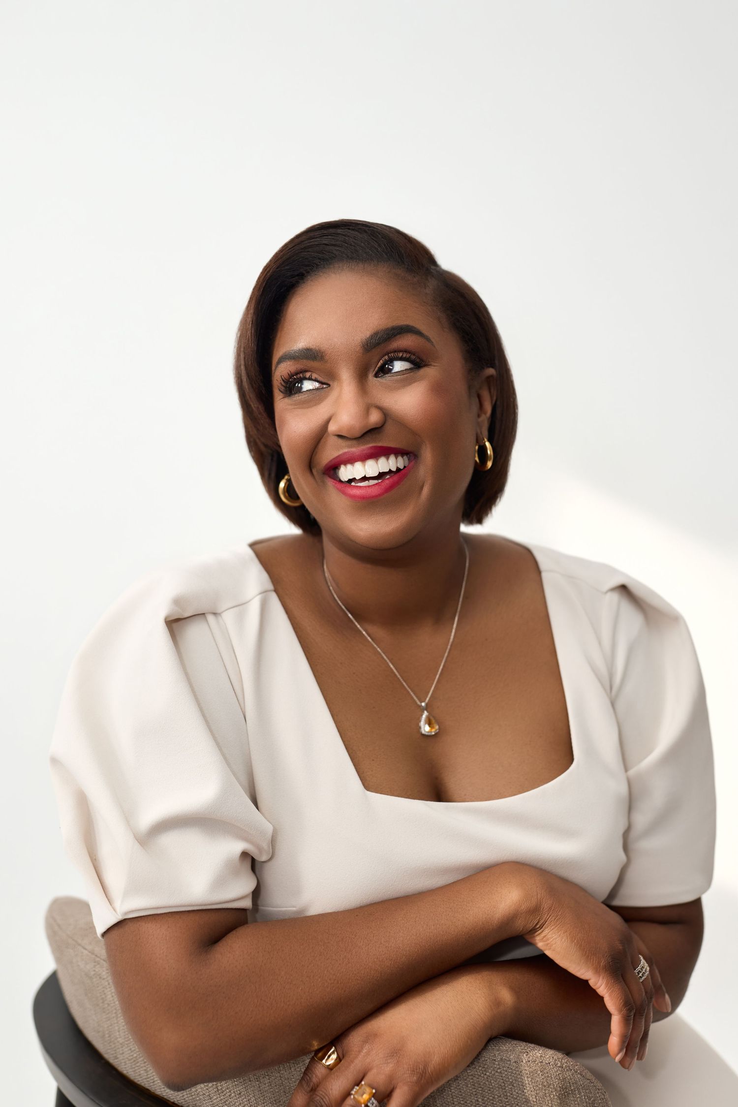 Portrait of someone wearing a cream-colored top with short puff sleeves and delicate jewelry against a white background.