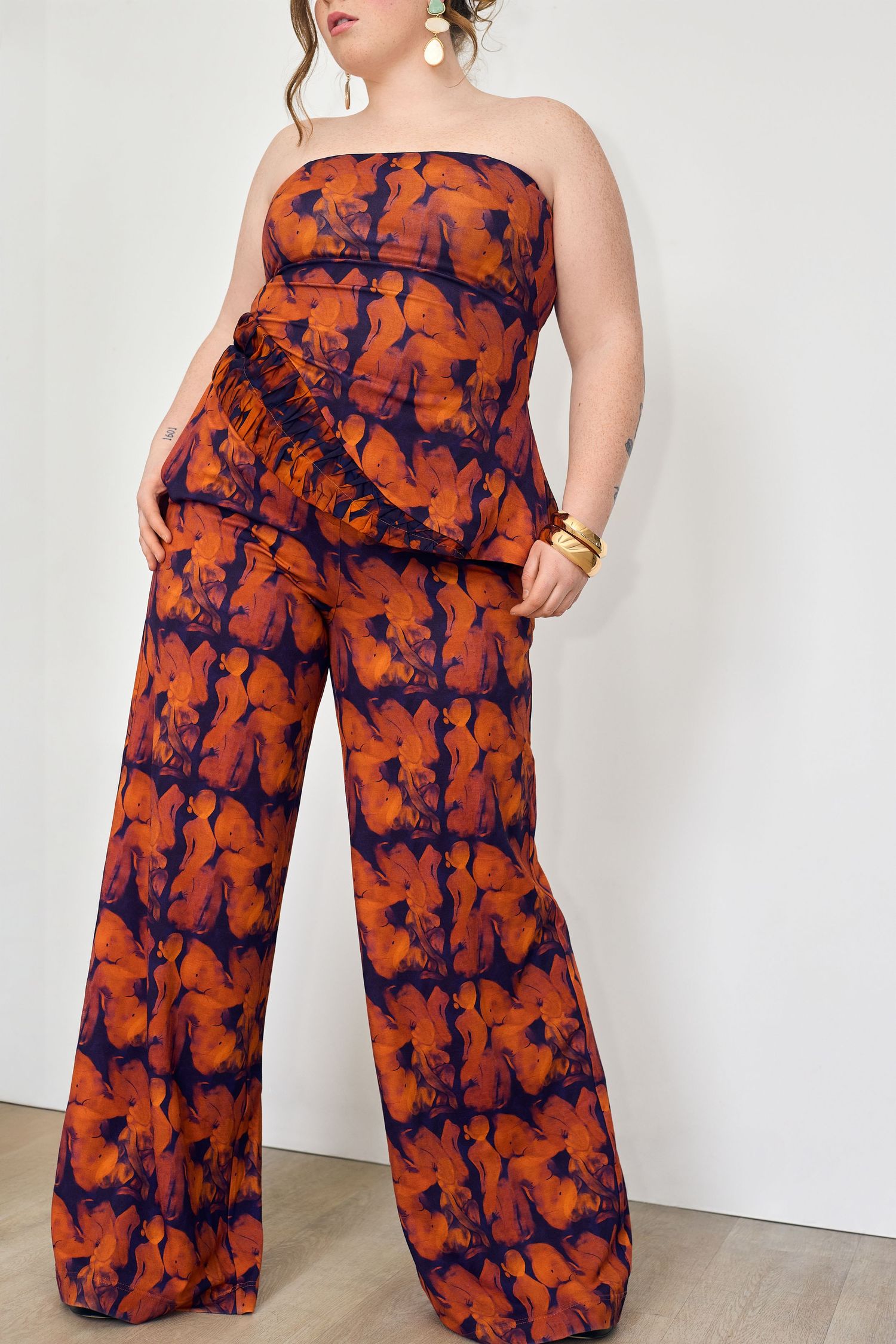 Plus size model wearing a strapless orange and navy floral tie-dye wide-leg jumpsuit with ruched waist detail.