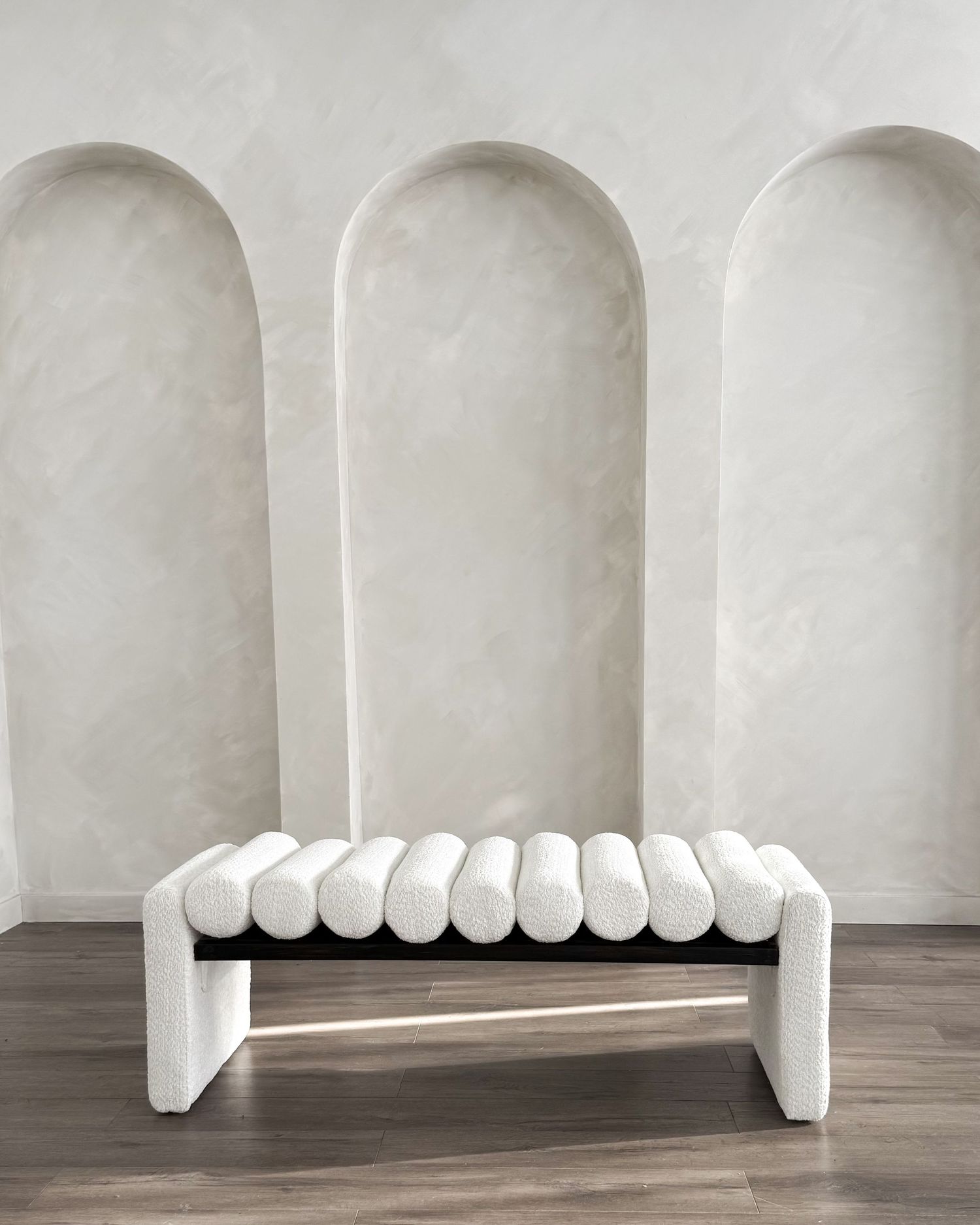 White boucle channeled bench with gold frame against arched plaster wall backdrop.