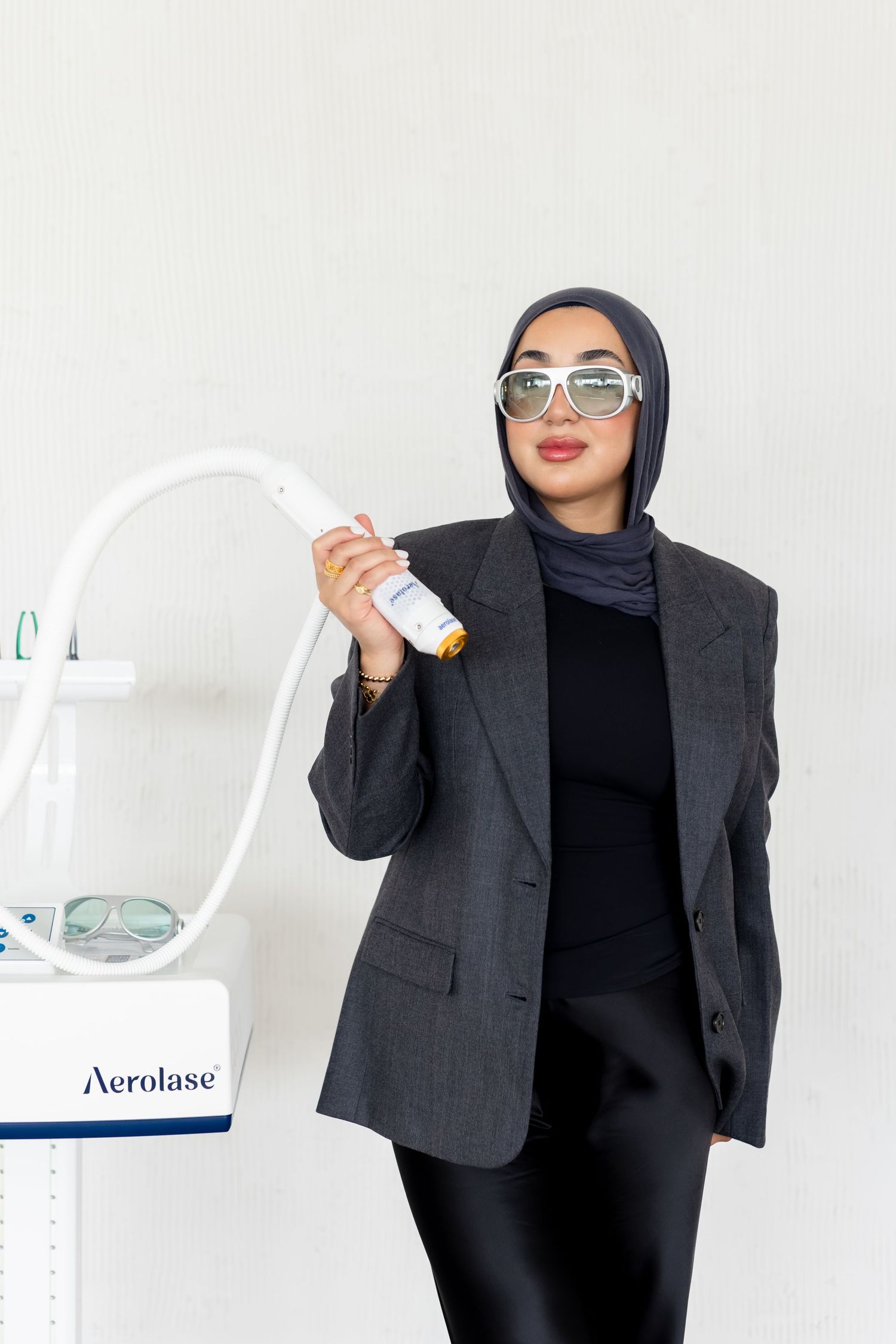 Professional wearing a dark blazer, hijab and sunglasses poses with an Aerolase medical device in a clinical setting.