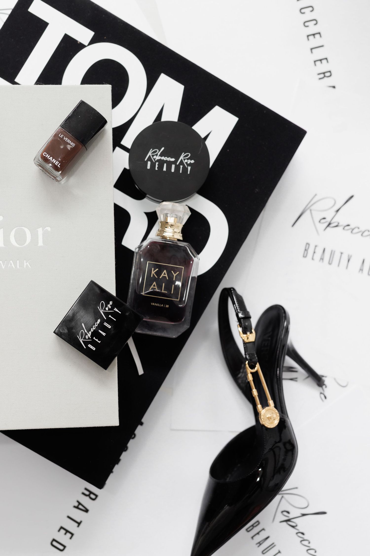 Flatlay of beauty products including perfume bottle, nail polish, and black patent leather heels on white and black backgrounds.