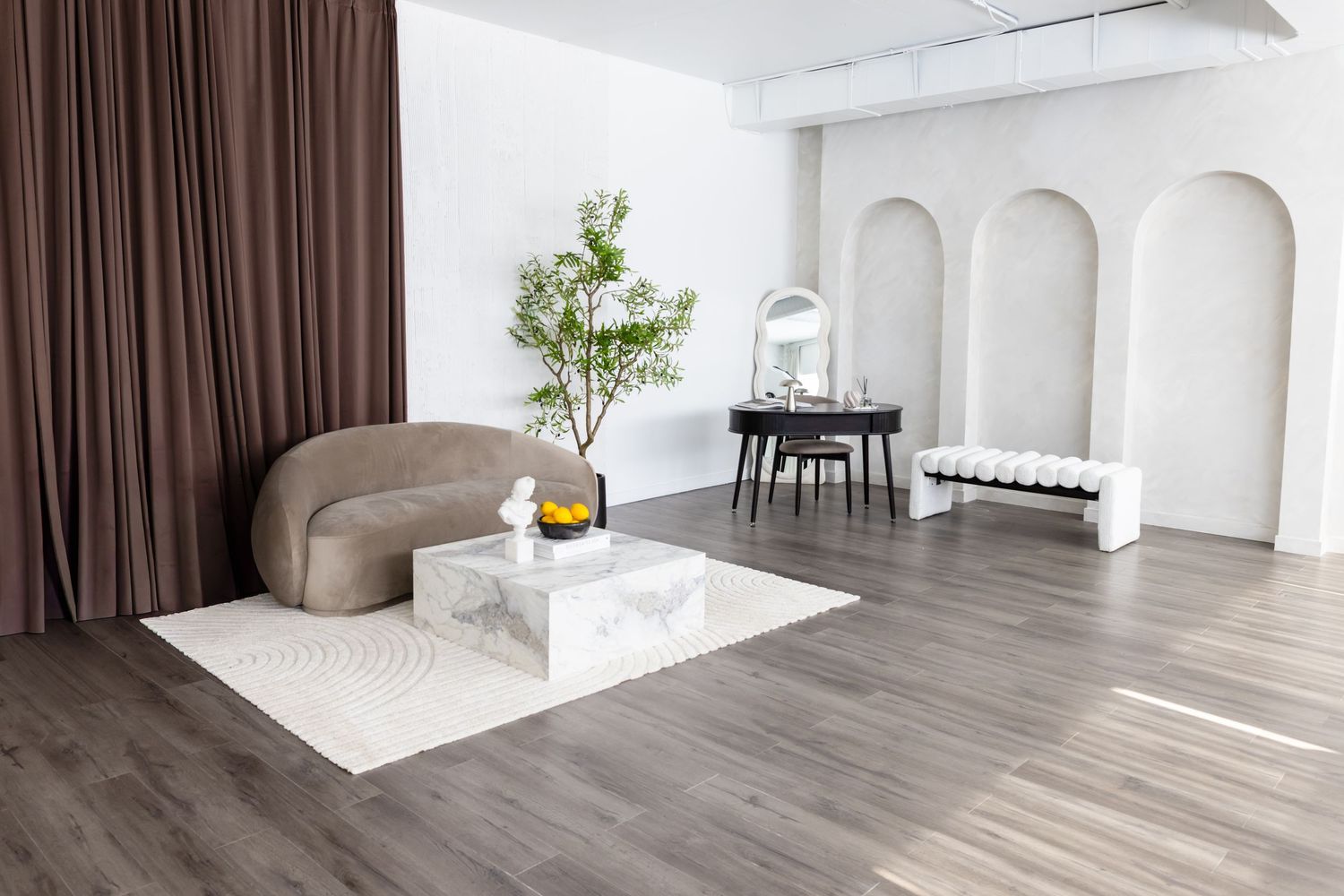 Modern minimalist studio space with arched walls, wooden floors, velvet chair, and marble coffee table.