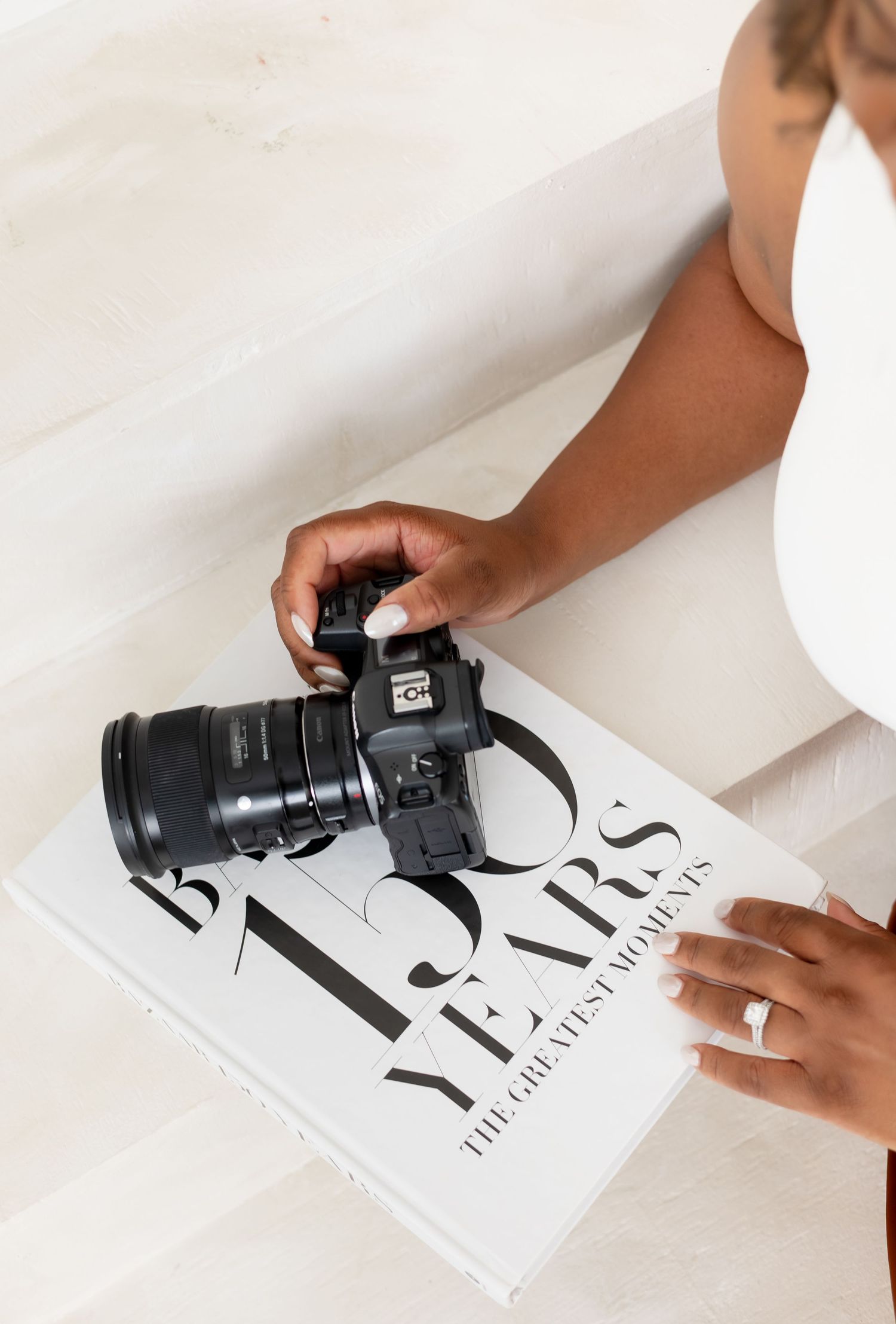 Hands placing a black DSLR camera on top of a white magazine or publication on a light colored surface.