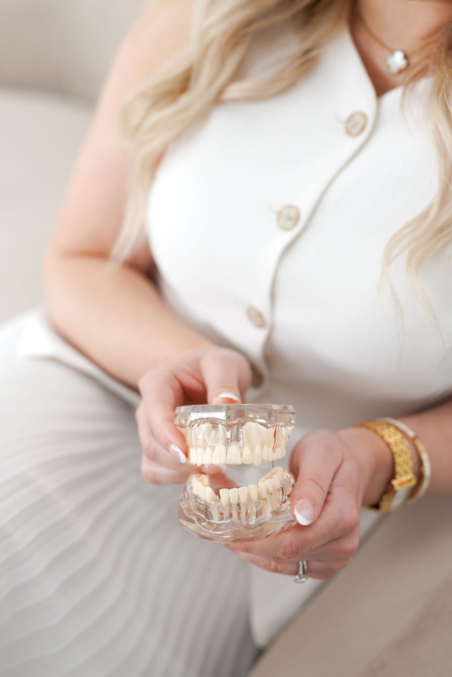 Blonde woman in white outfit holding a dental jaw model with teeth, showcasing dental prosthetics in a clinical setting.