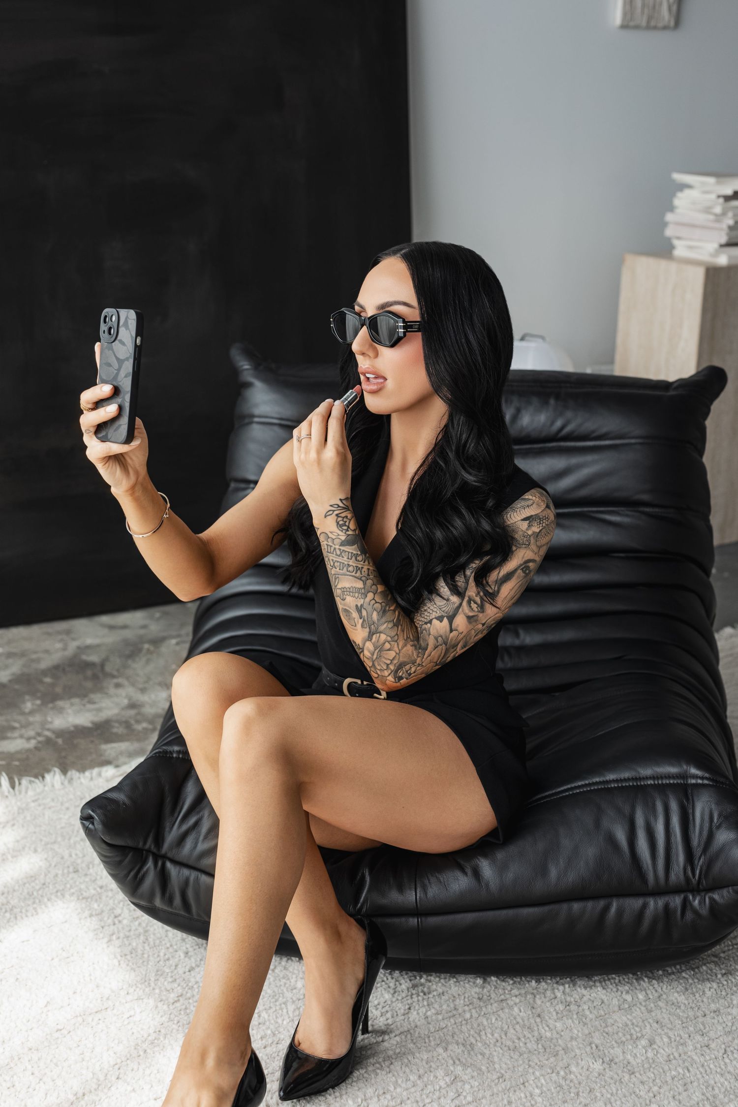 Stylish portrait on black leather chair showing tattoo sleeve and sunglasses.