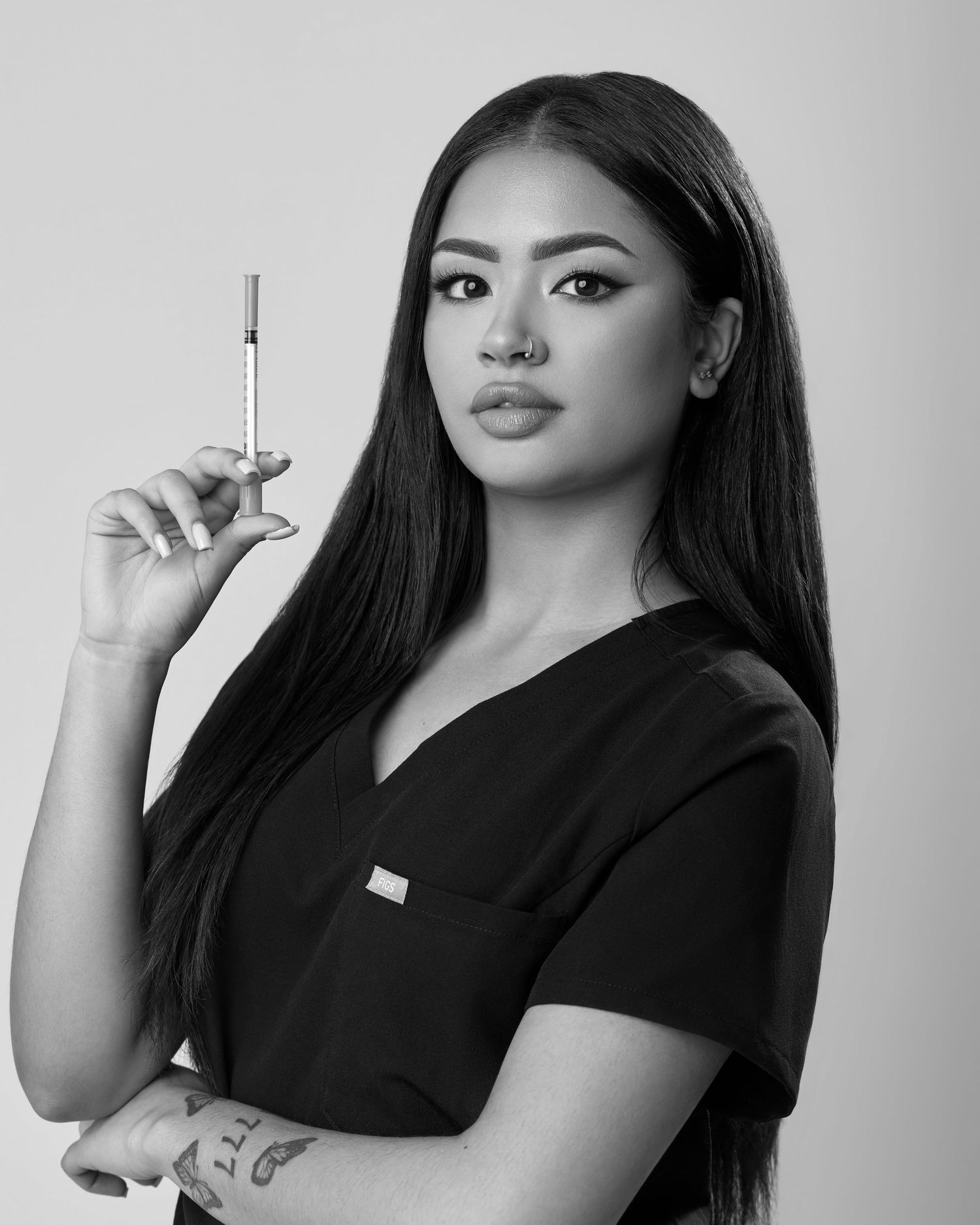 Black and white portrait of a female medical professional in scrubs holding a syringe with long dark hair.