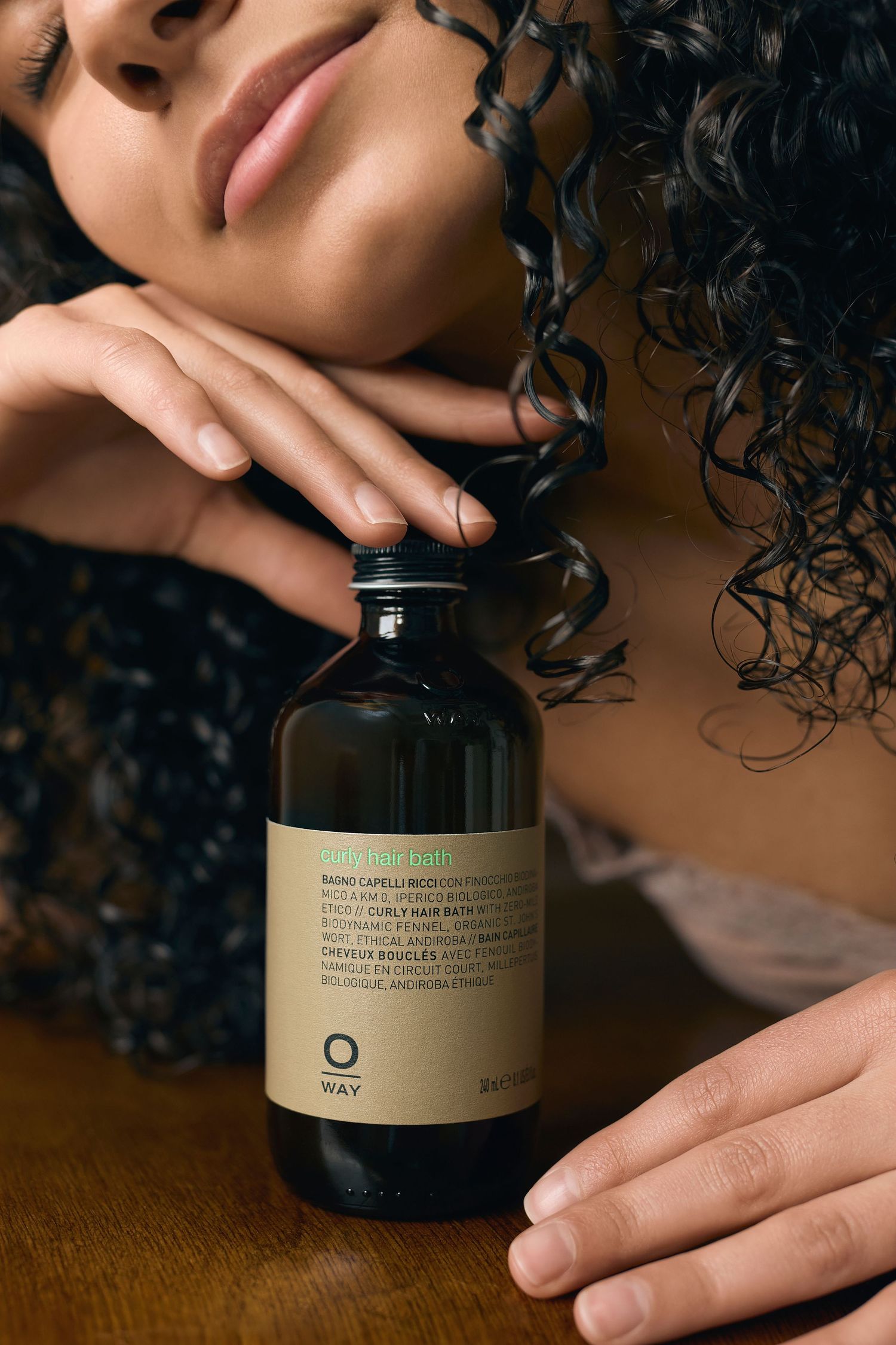 Hands holding and examining a dark glass skincare product container on a wooden surface.