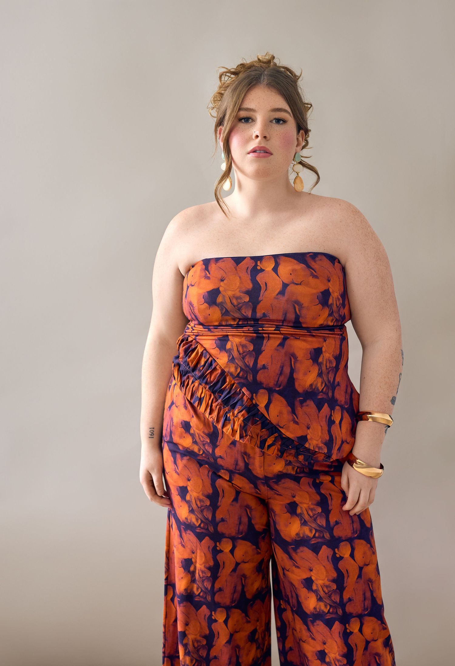 Woman wearing a strapless orange and navy floral print jumpsuit with fringe detail and wide-leg pants.