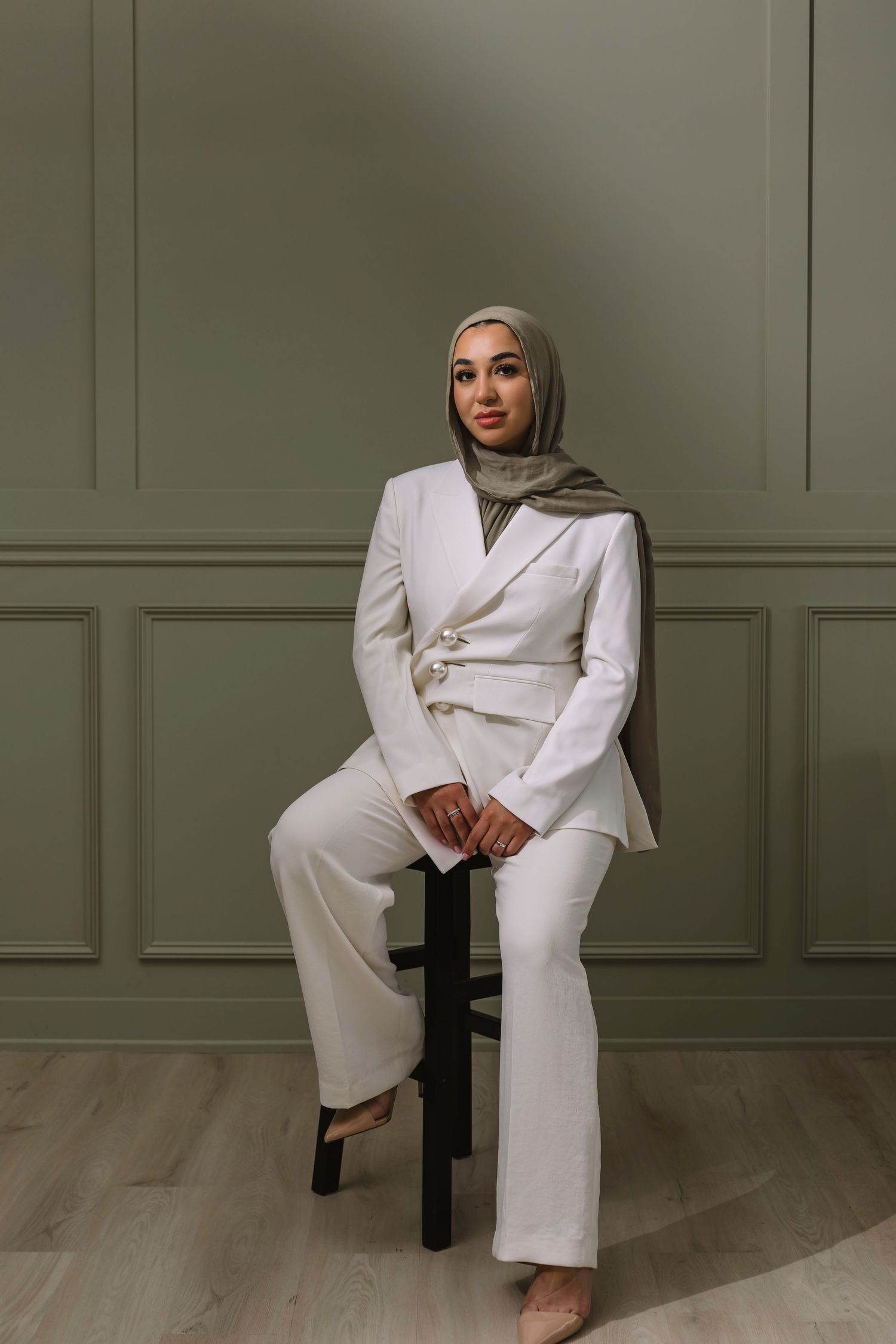 Elegant white pantsuit and sage hijab outfit styled in modern professional setting with minimalist backdrop and wooden floor.