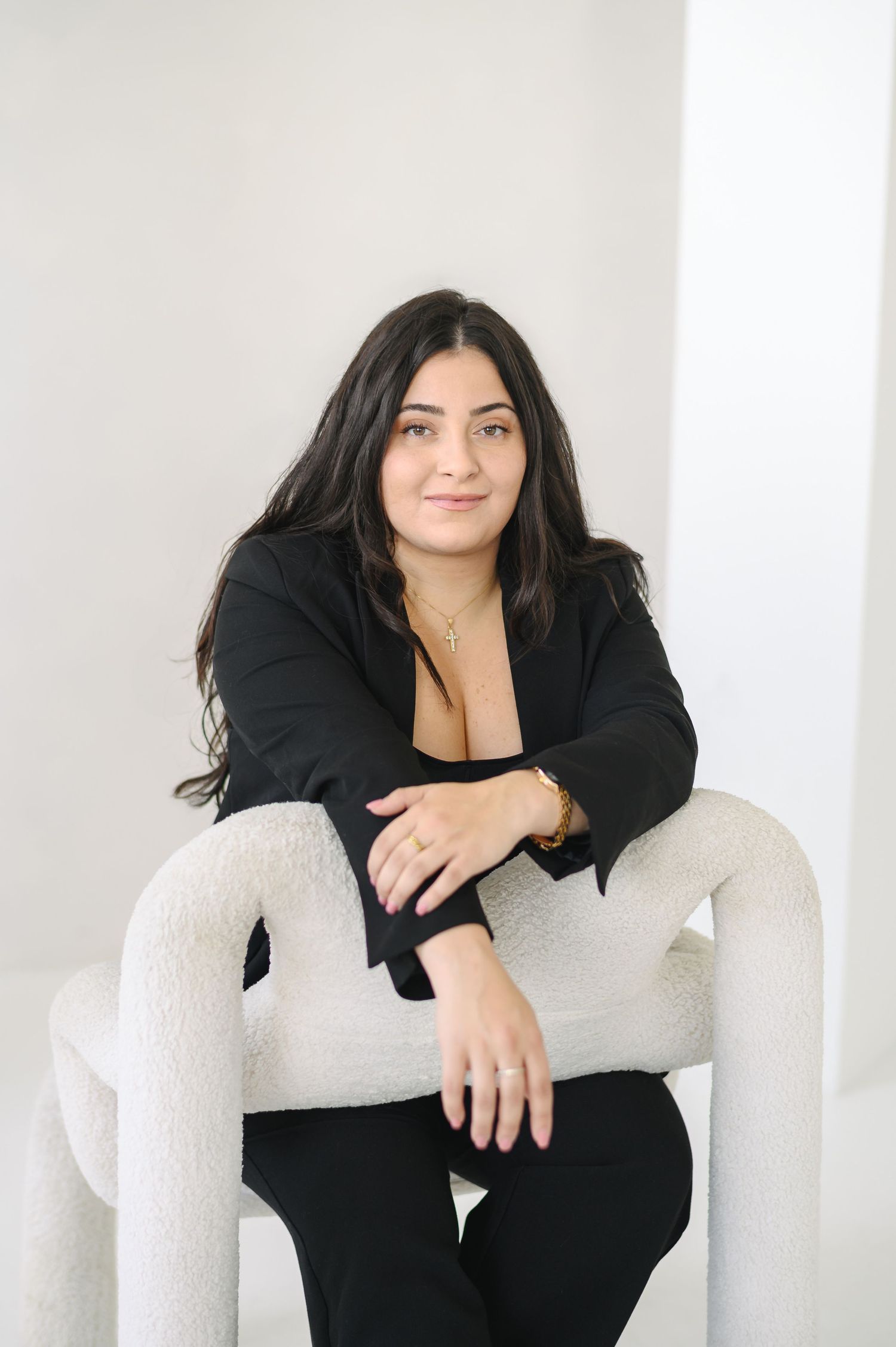 A figure in black clothing poses on a white armchair in a minimalist studio setting, shown in three different positions.
