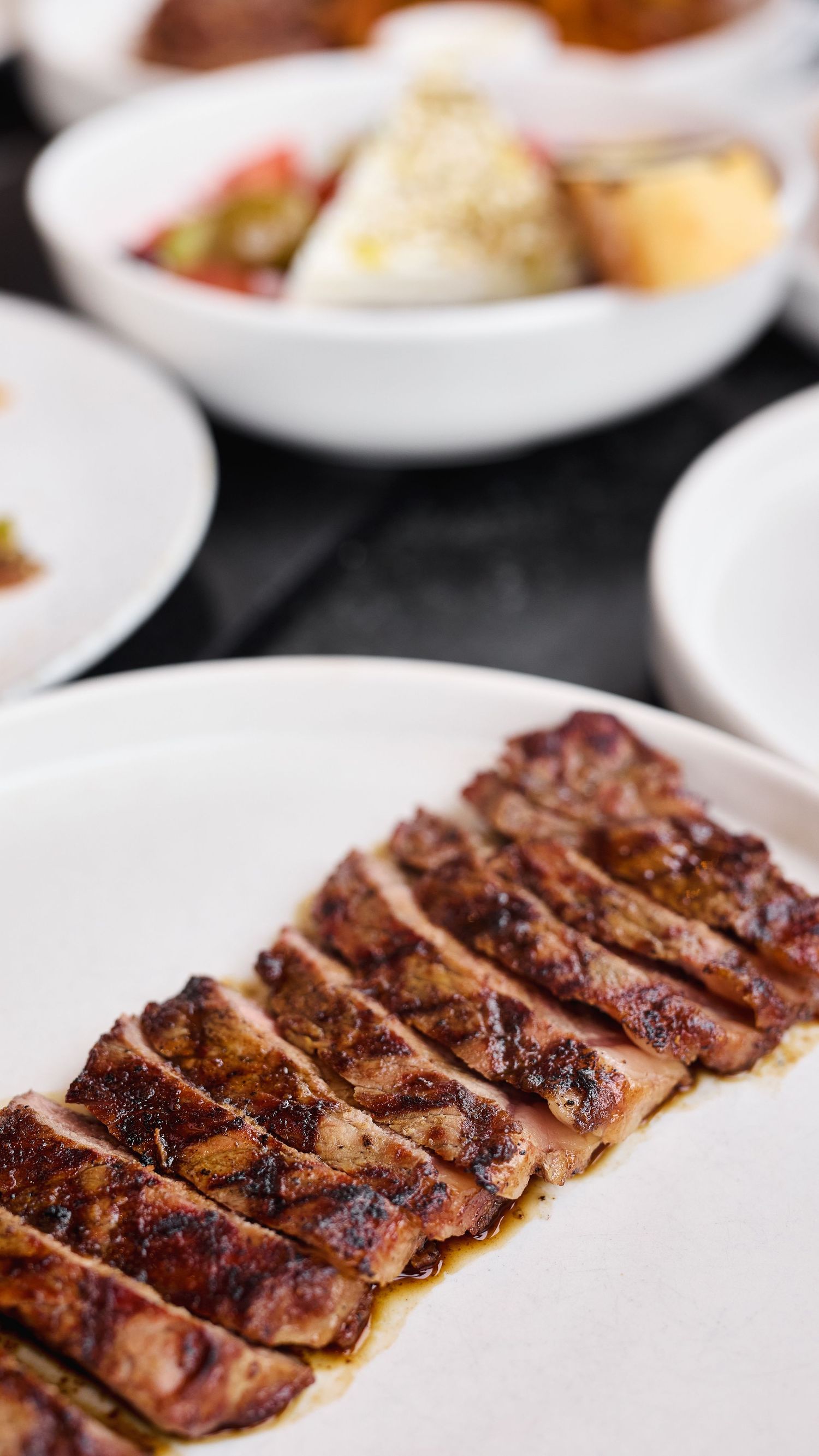 Grilled sliced steak with charred edges served on white plates in a restaurant setting.