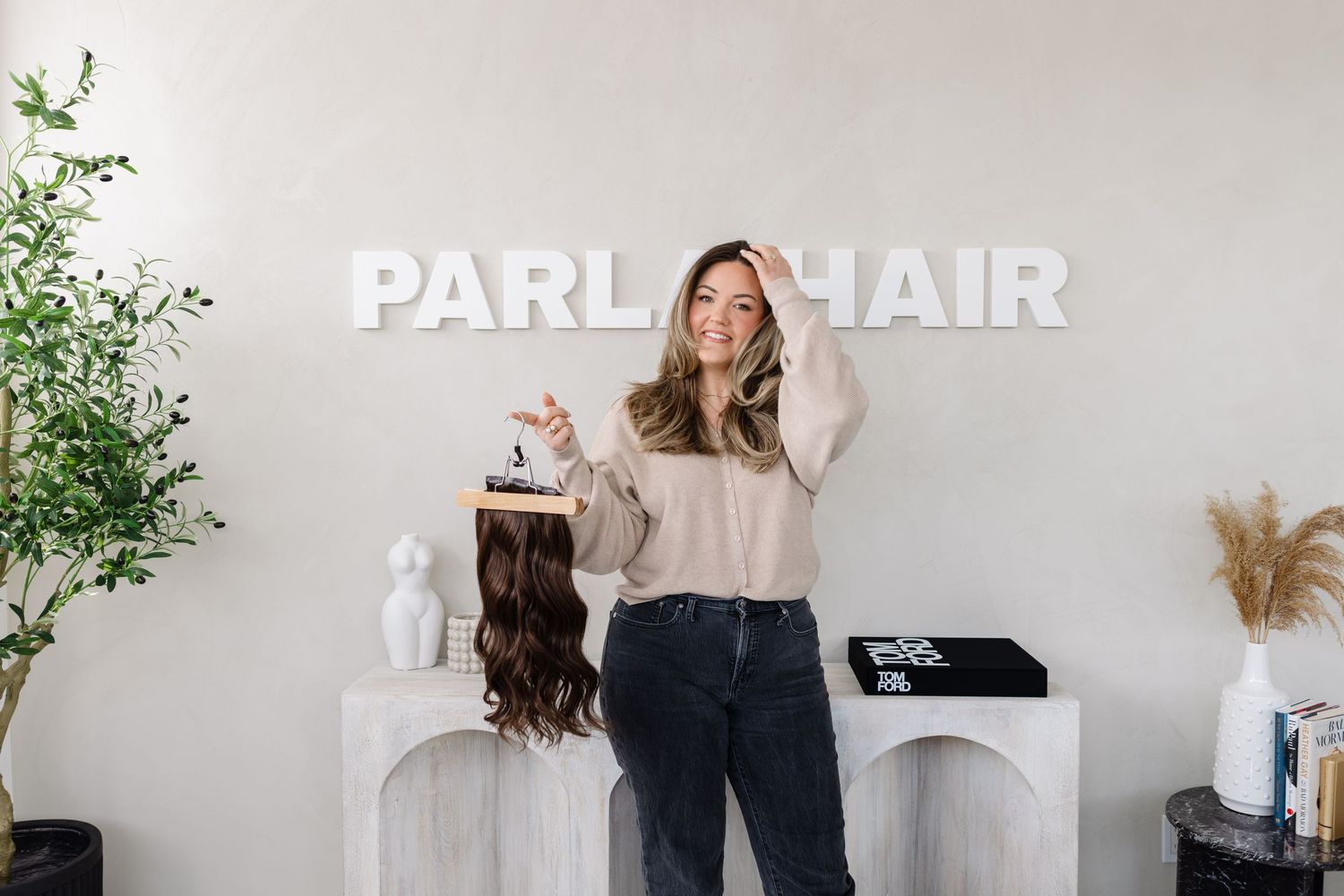 Hair stylist posing in modern salon interior with white Parlor Hair signage and minimalist decor.