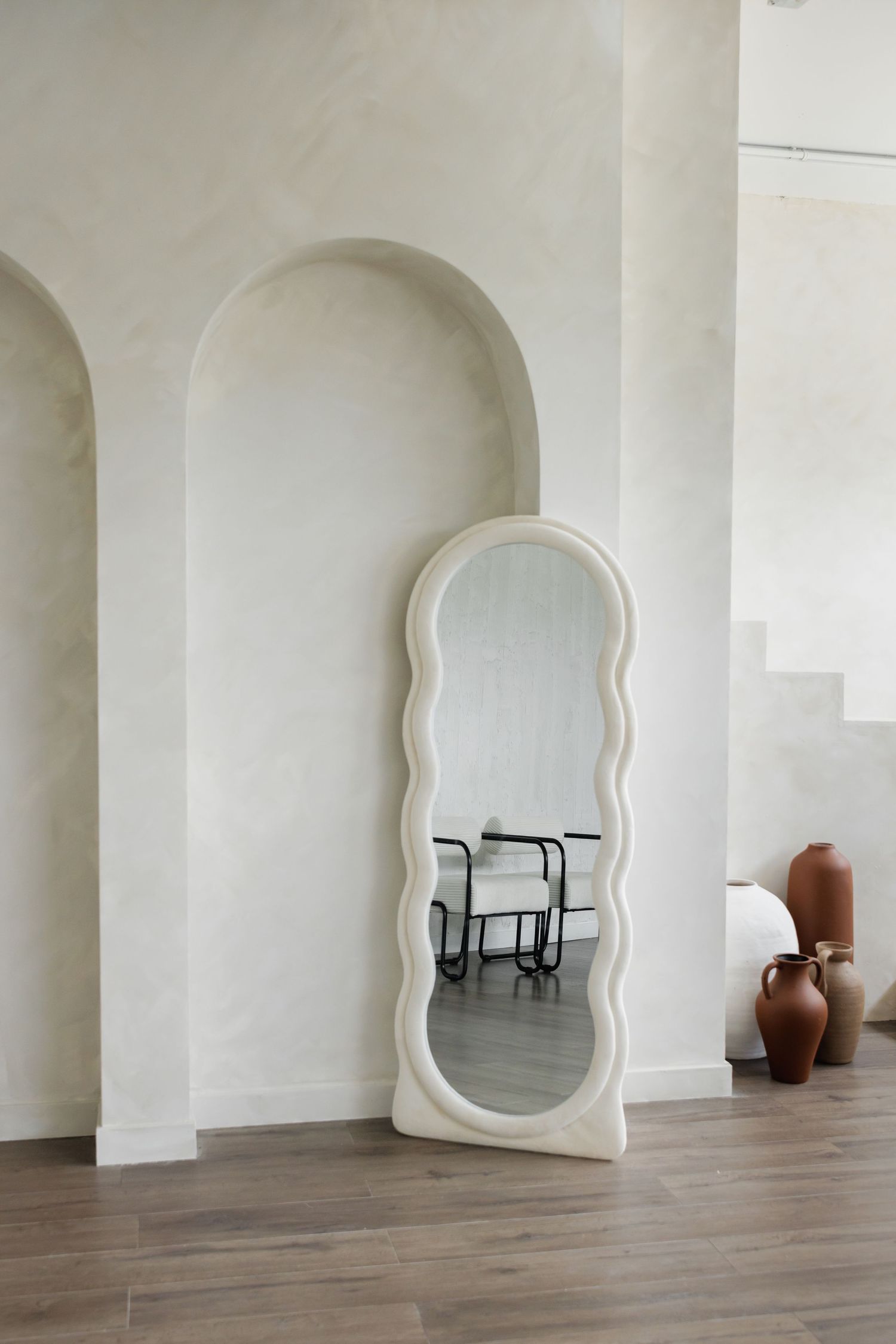 Clean white interior space with arched doorways and decorative floor mirror.