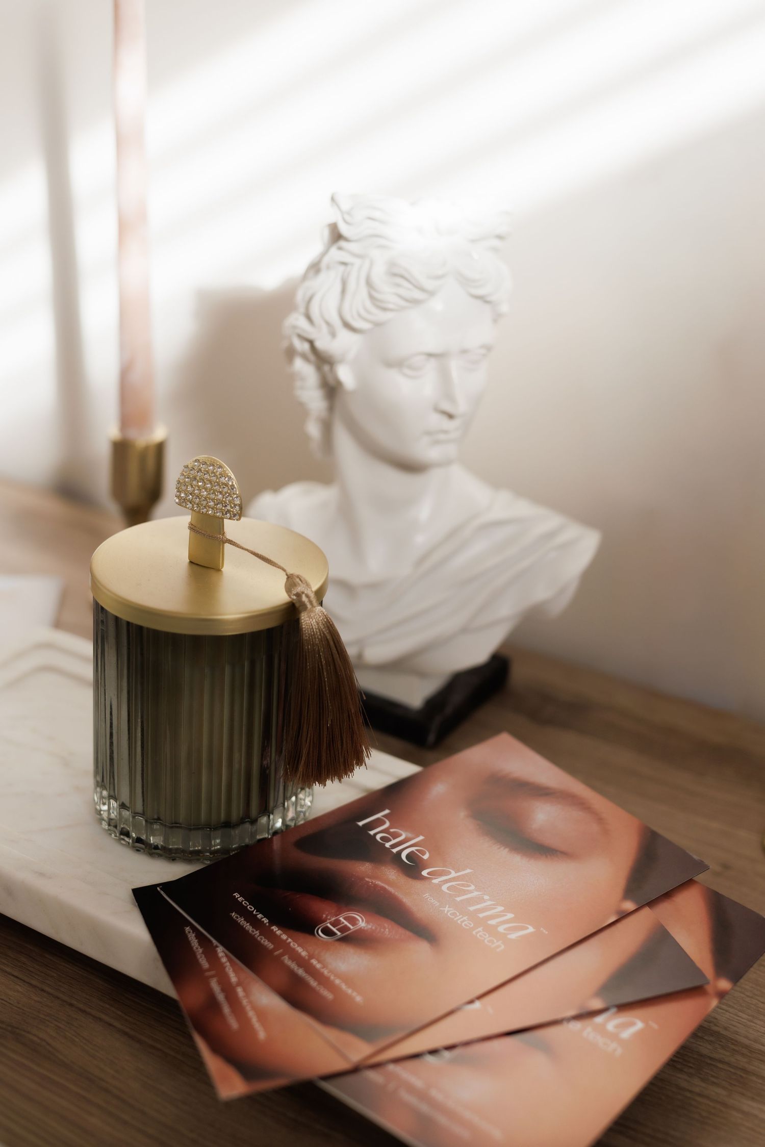 Elegant still life composition with magazines, decorative candles, and a white classical bust sculpture on wooden surface.