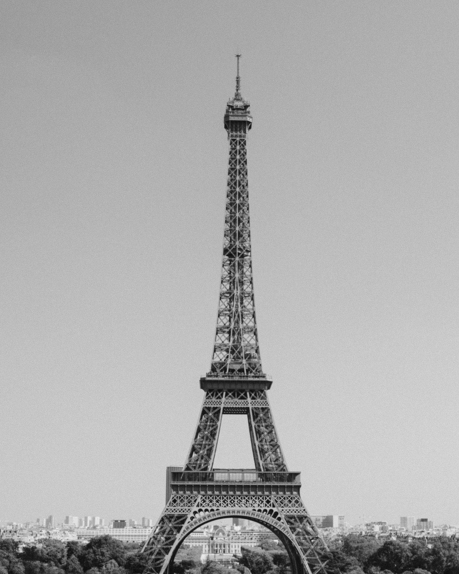 Black and white photo of the Eiffel Tower in Paris, France, standing tall against a clear sky.