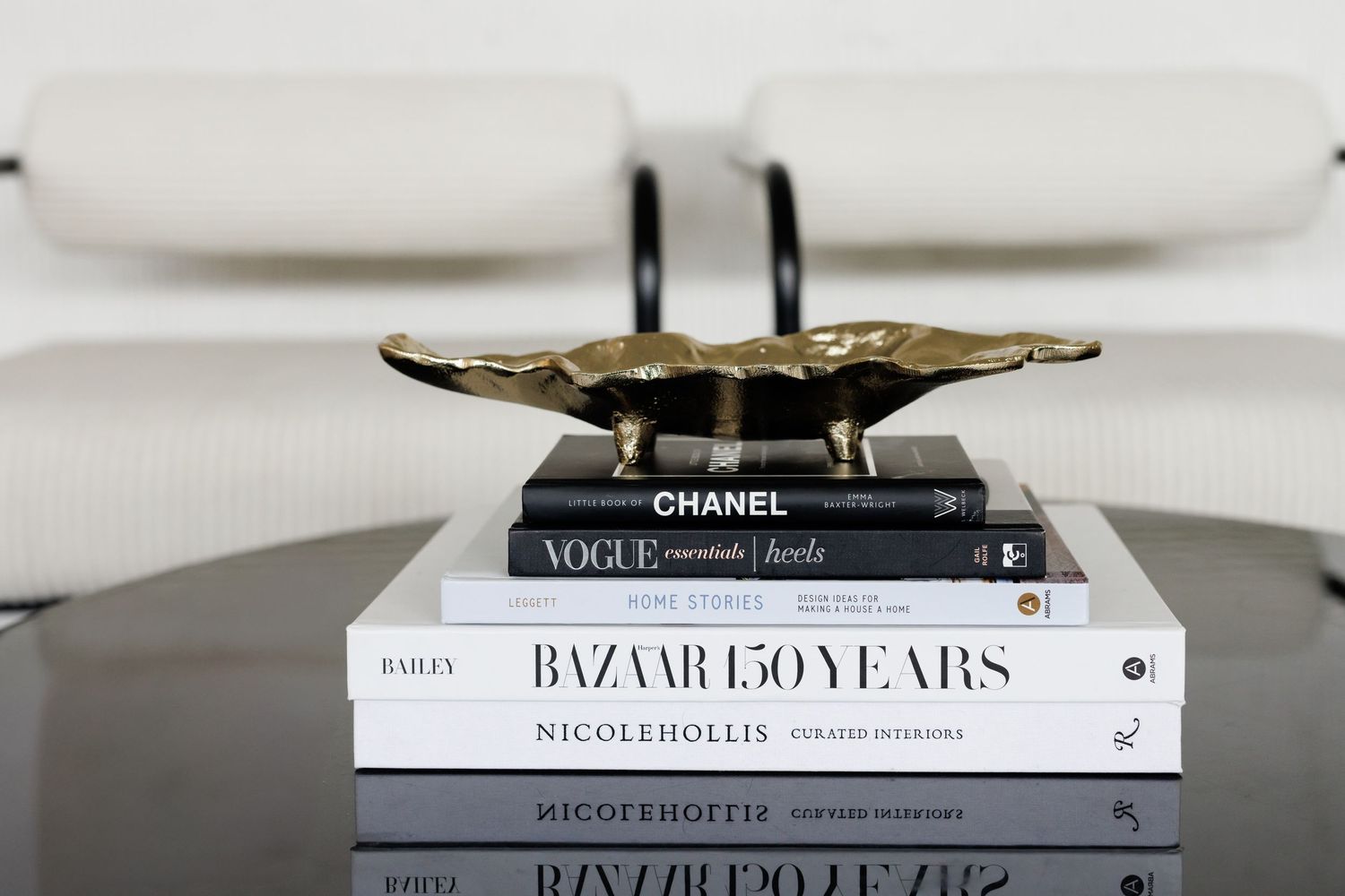 Stack of fashion books including Chanel and Bazaar with decorative gold object on top.