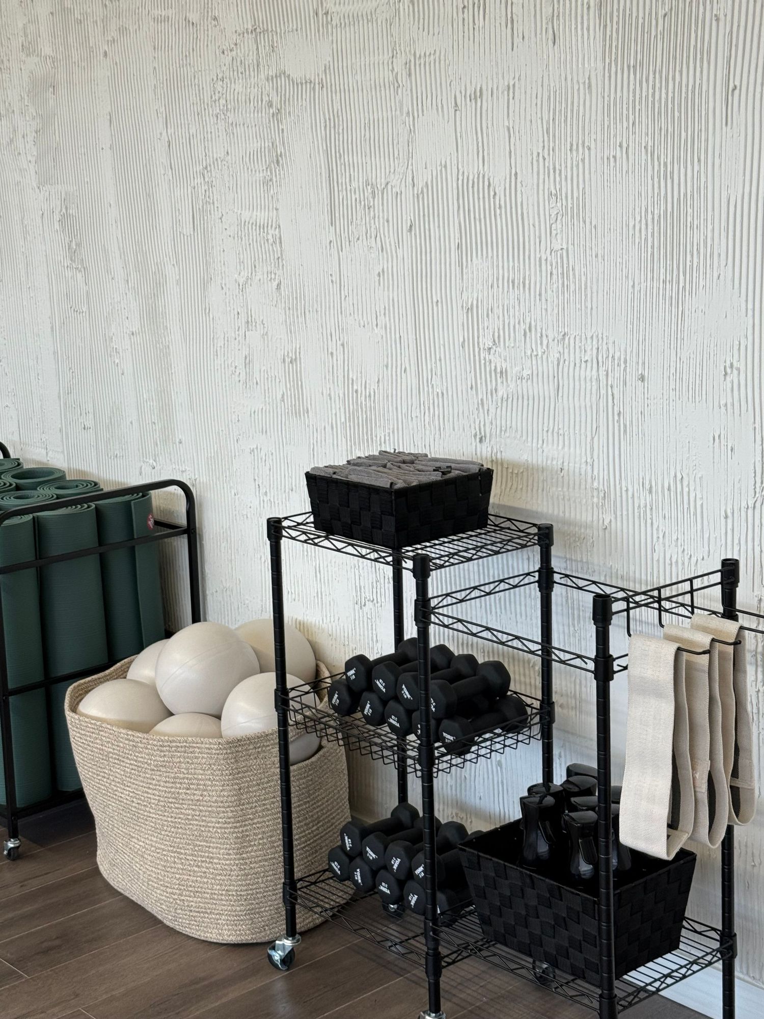 Organized storage area with black metal shelving units and beige storage basket against textured white wall.