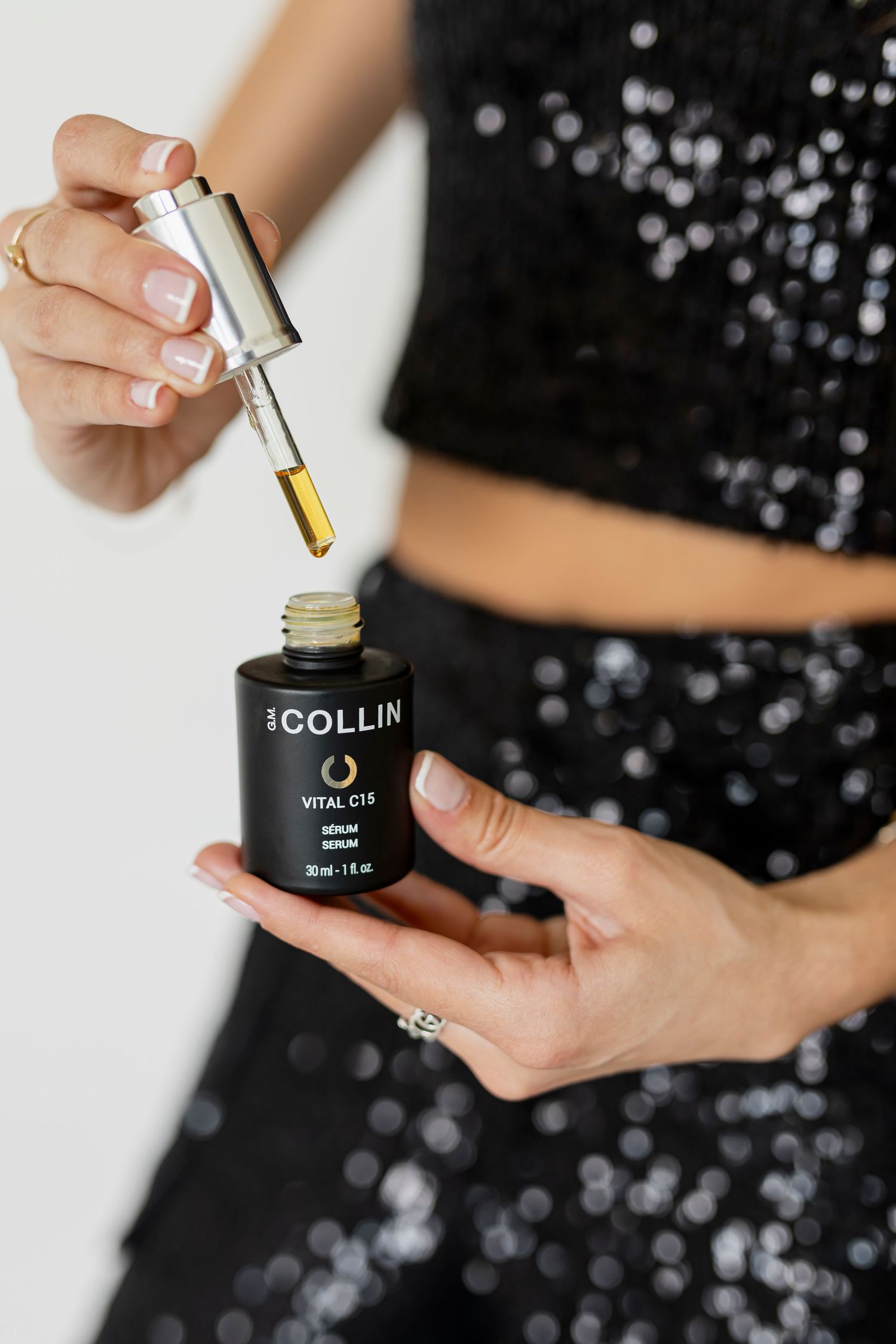 Hands opening a black jar of skincare product against a sparkly dark background with product droppers and beauty jars.
