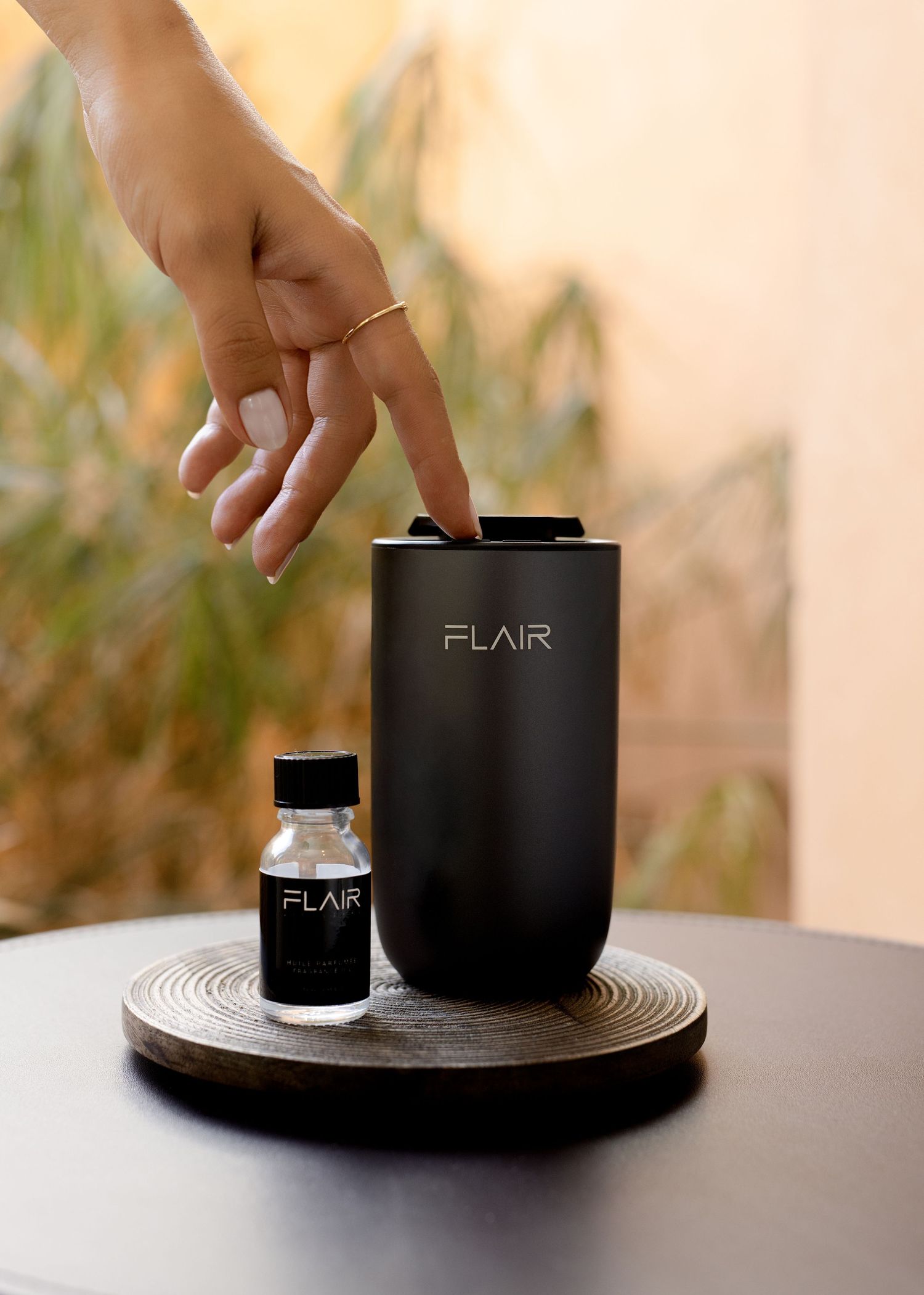 Hand pressing button on Flair black aroma diffuser beside essential oil bottle on wooden tray.