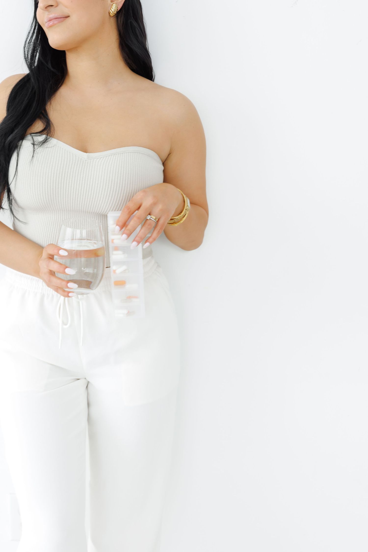Woman in white outfit holding glass of water against minimalist background.