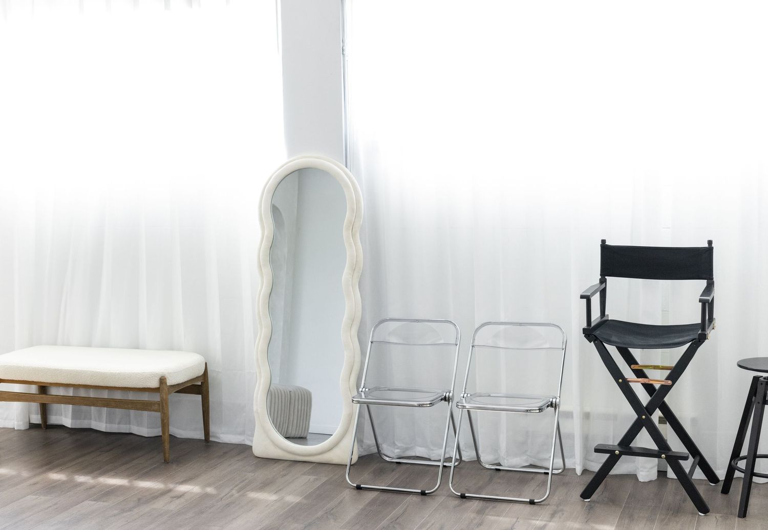 Interior scene with a vintage white mirror, folding chairs, and a tall director's chair against a minimalist white wall.