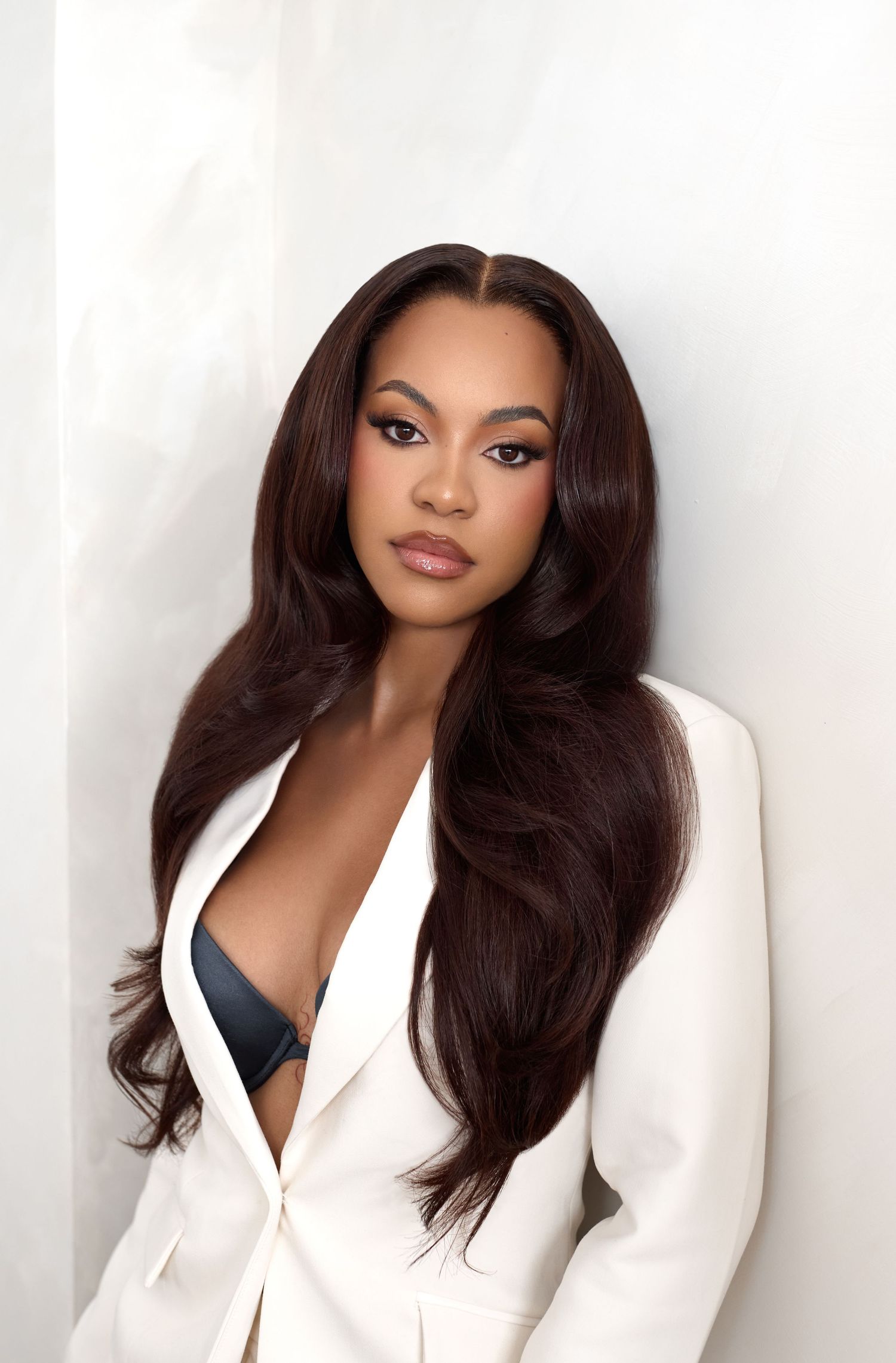 Professional portrait of a model wearing a white blazer against a light background with flowing dark hair.