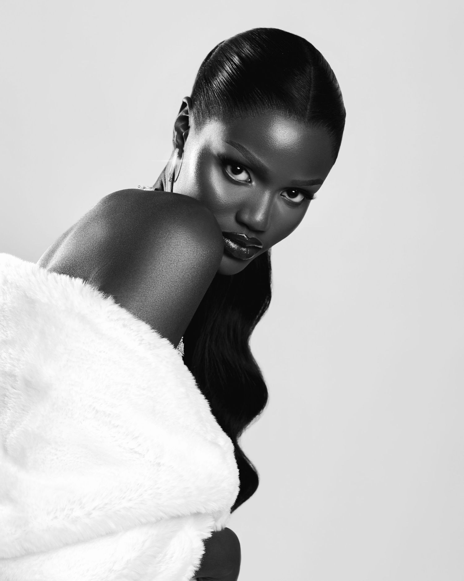 A striking black and white fashion portrait shows a figure wearing a white feathered accessory against a light background.