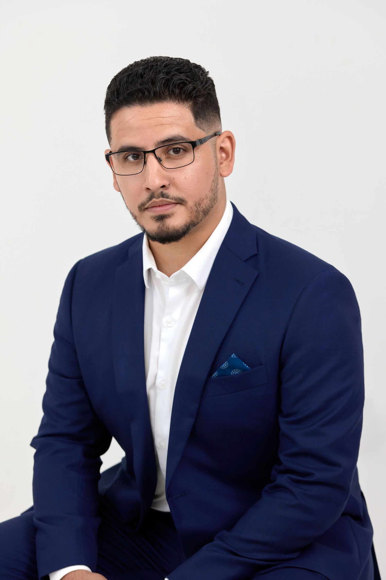 Professional headshot portrait of a person in a navy blue suit and white shirt against a plain white background.