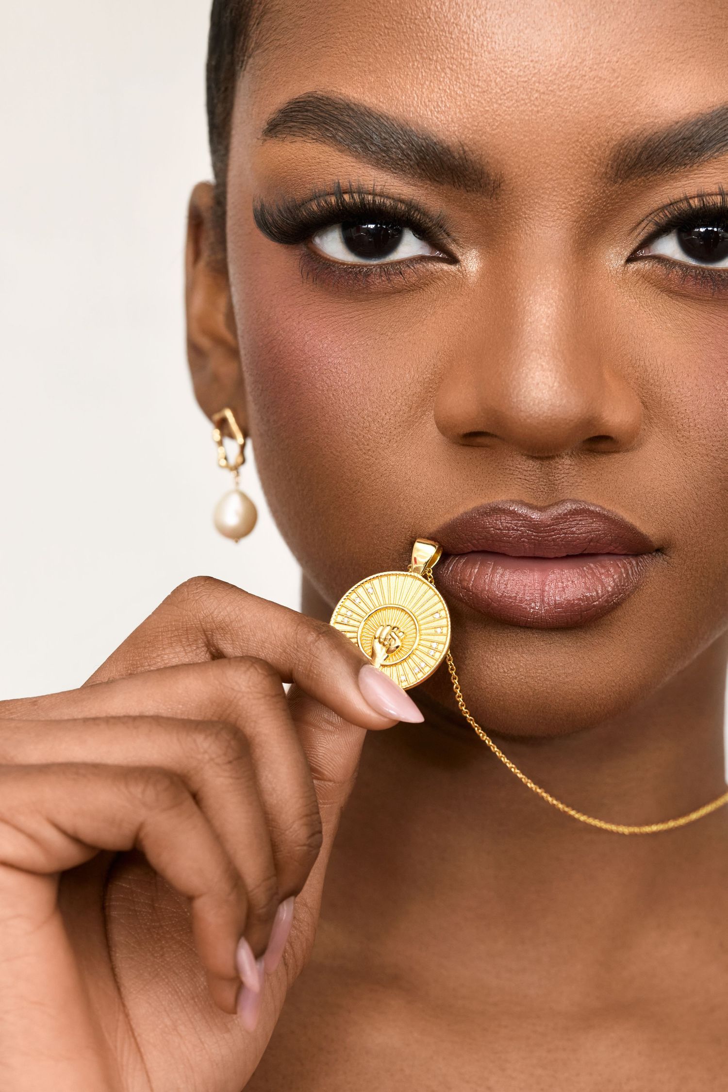 Close-up beauty shot showcasing gold jewelry and flawless makeup with warm earth tones.