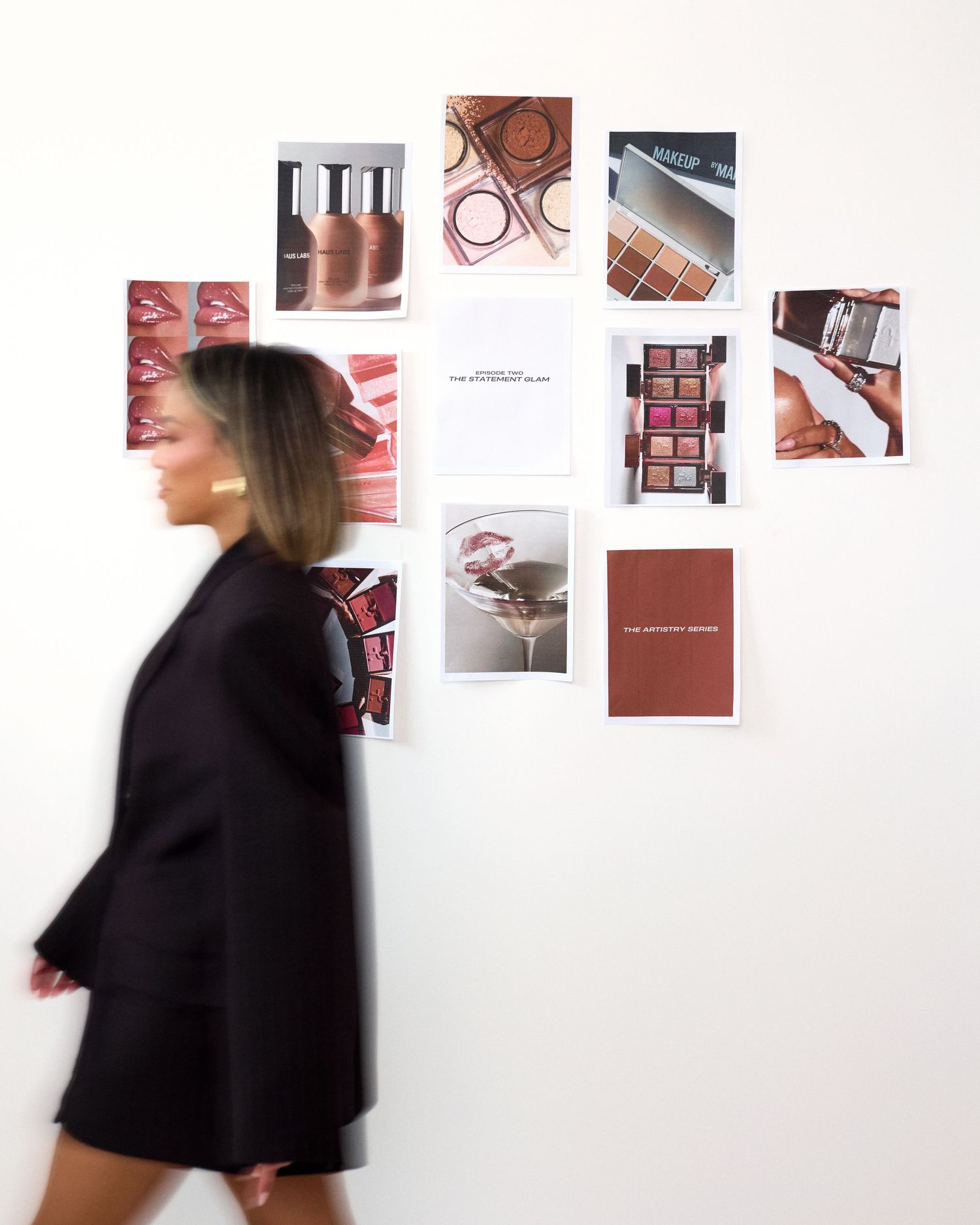 A person in black clothing moves past a white wall displaying artistic photographs and design elements.