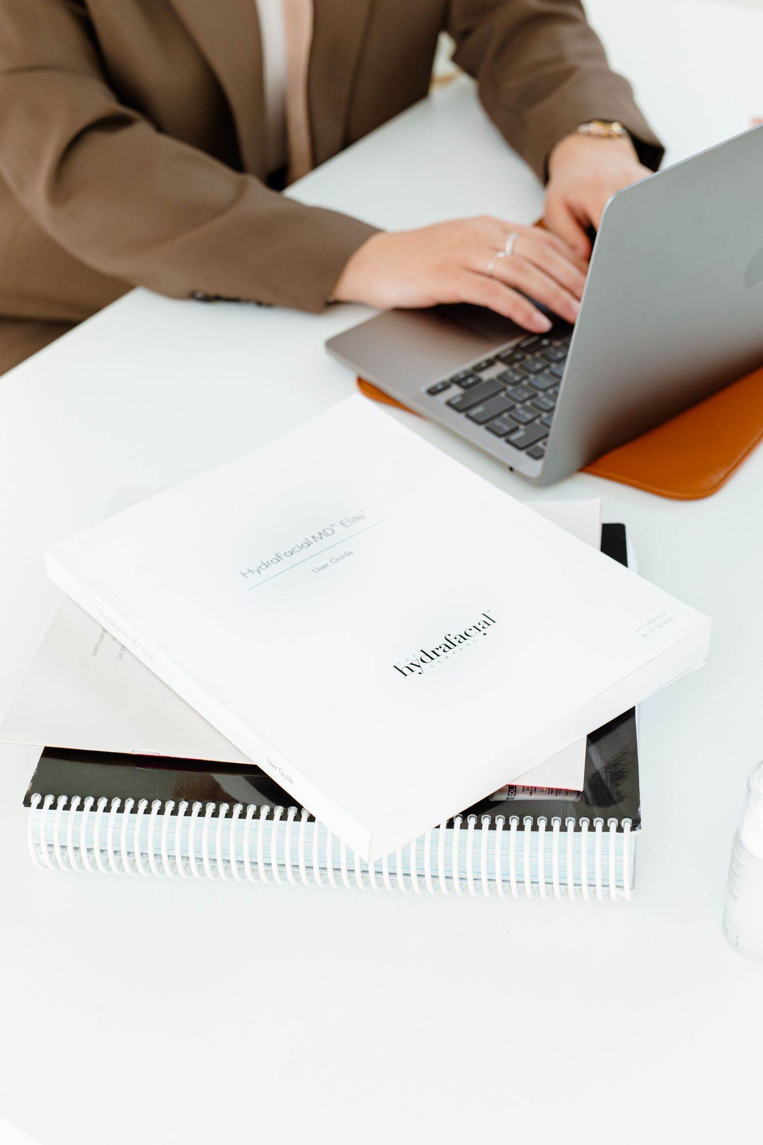 Person typing on laptop with white notebooks and business materials on clean white desk surface.