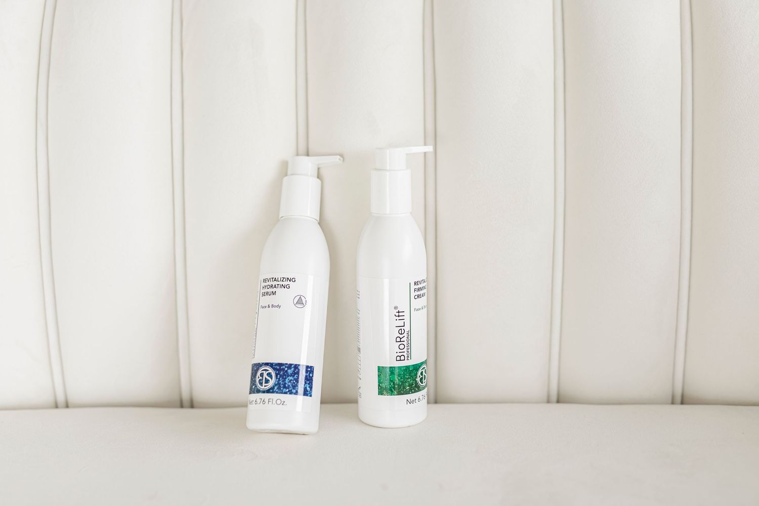 Two white plastic bottles with blue and green labels sit on a white paneled surface against a light wall.