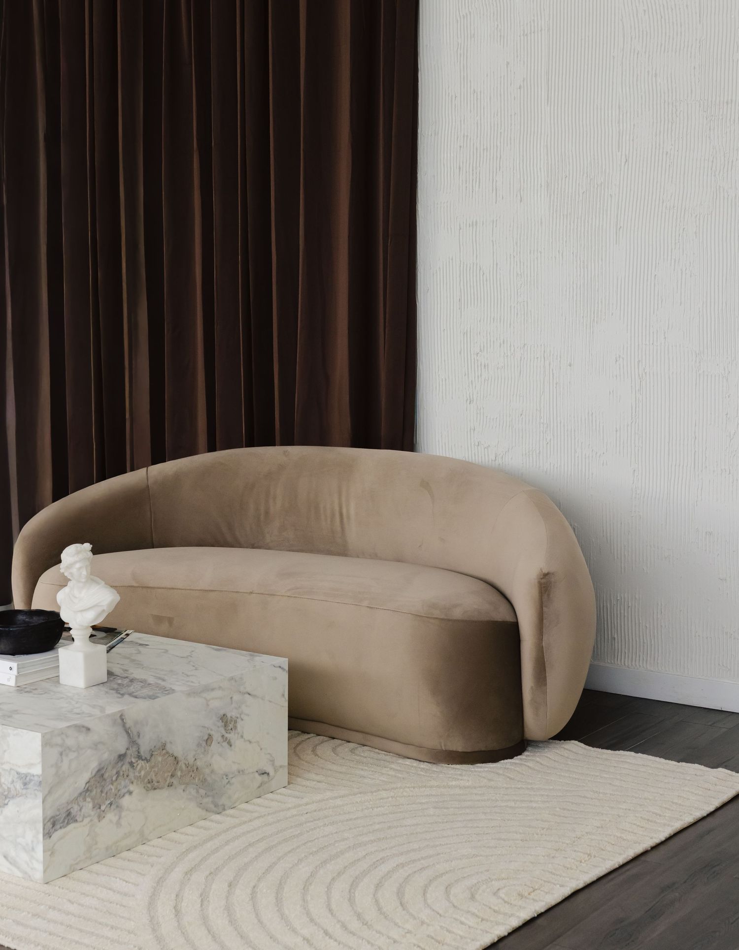 Modern curved beige sofa with integrated marble platform creates a sculptural statement piece in minimalist interior.