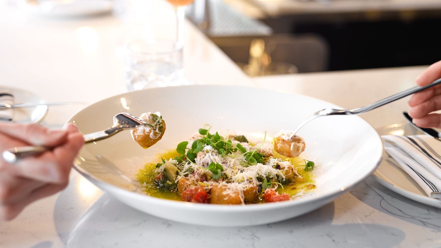 Elegant plated gnocchi dish with fresh herbs, cherry tomatoes, and Parmesan in a white bowl at a fine dining restaurant.
