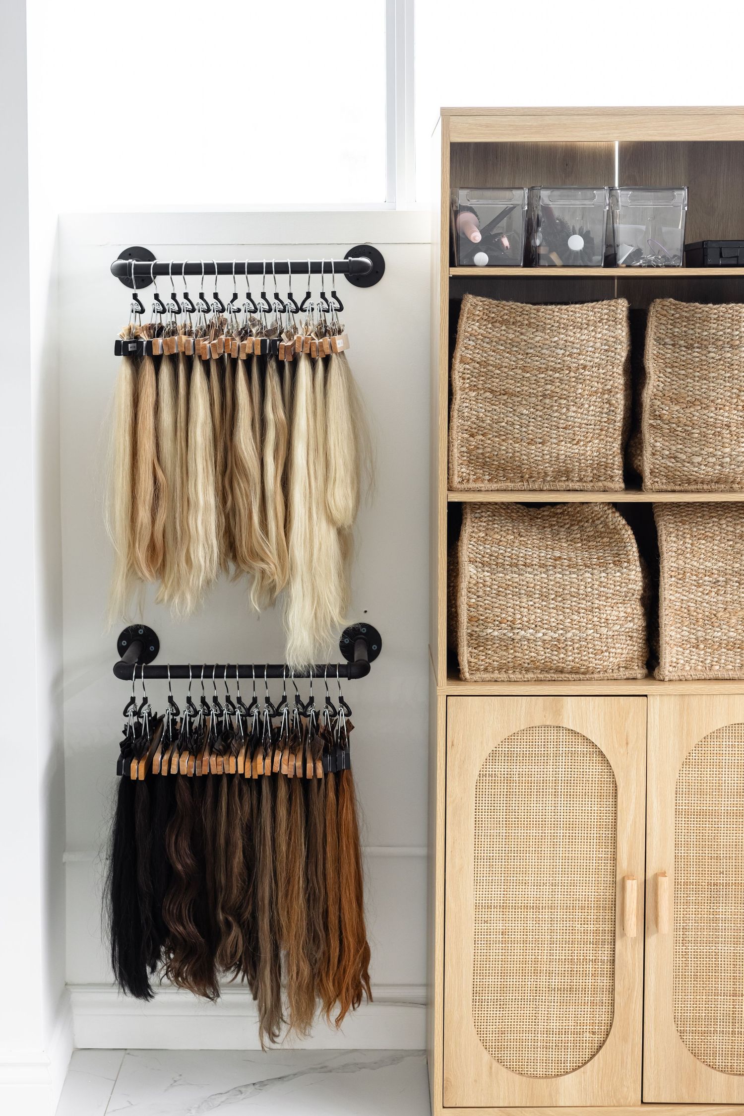 Hair extension display wall with woven baskets and rattan doors showcasing various colored extensions on black hanging rods.