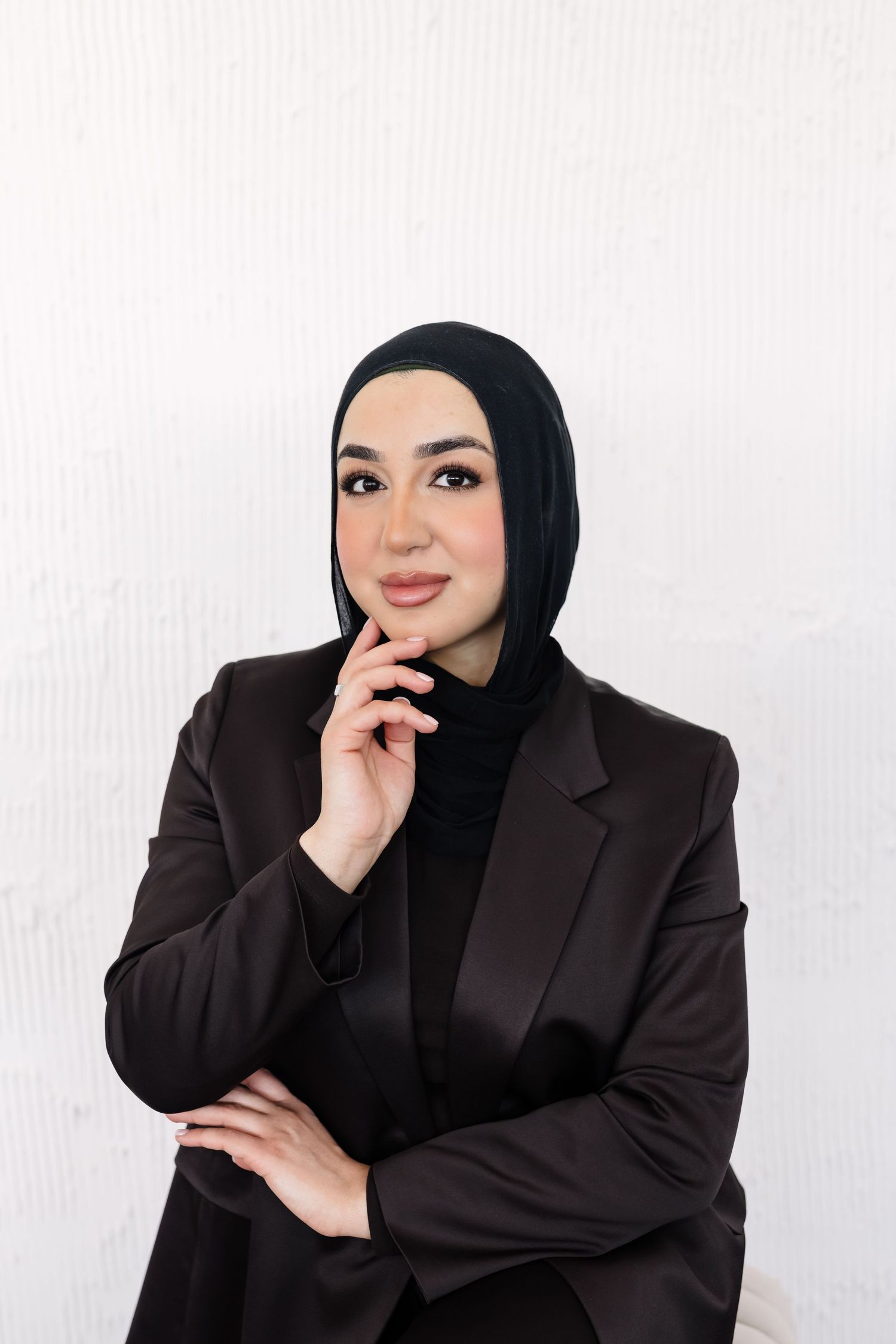 Woman in black hijab and blazer poses confidently against white background in professional photoshoot series.